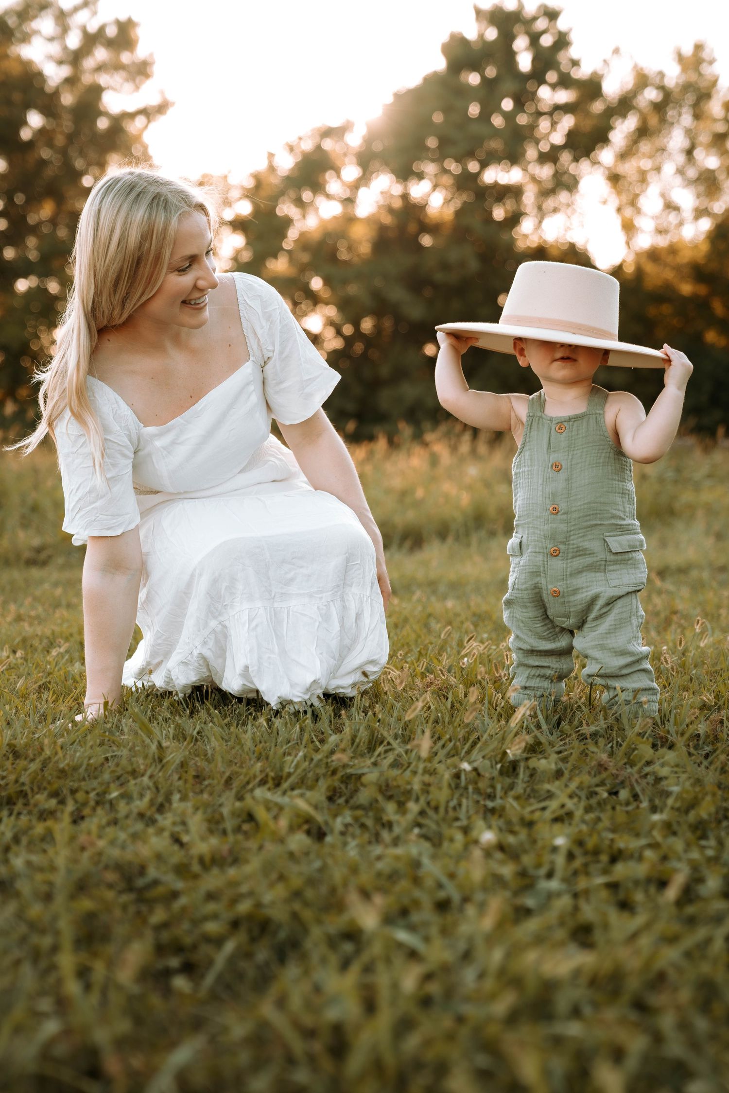 Playful couple sits together in grassy field during golden hour photoshoot.