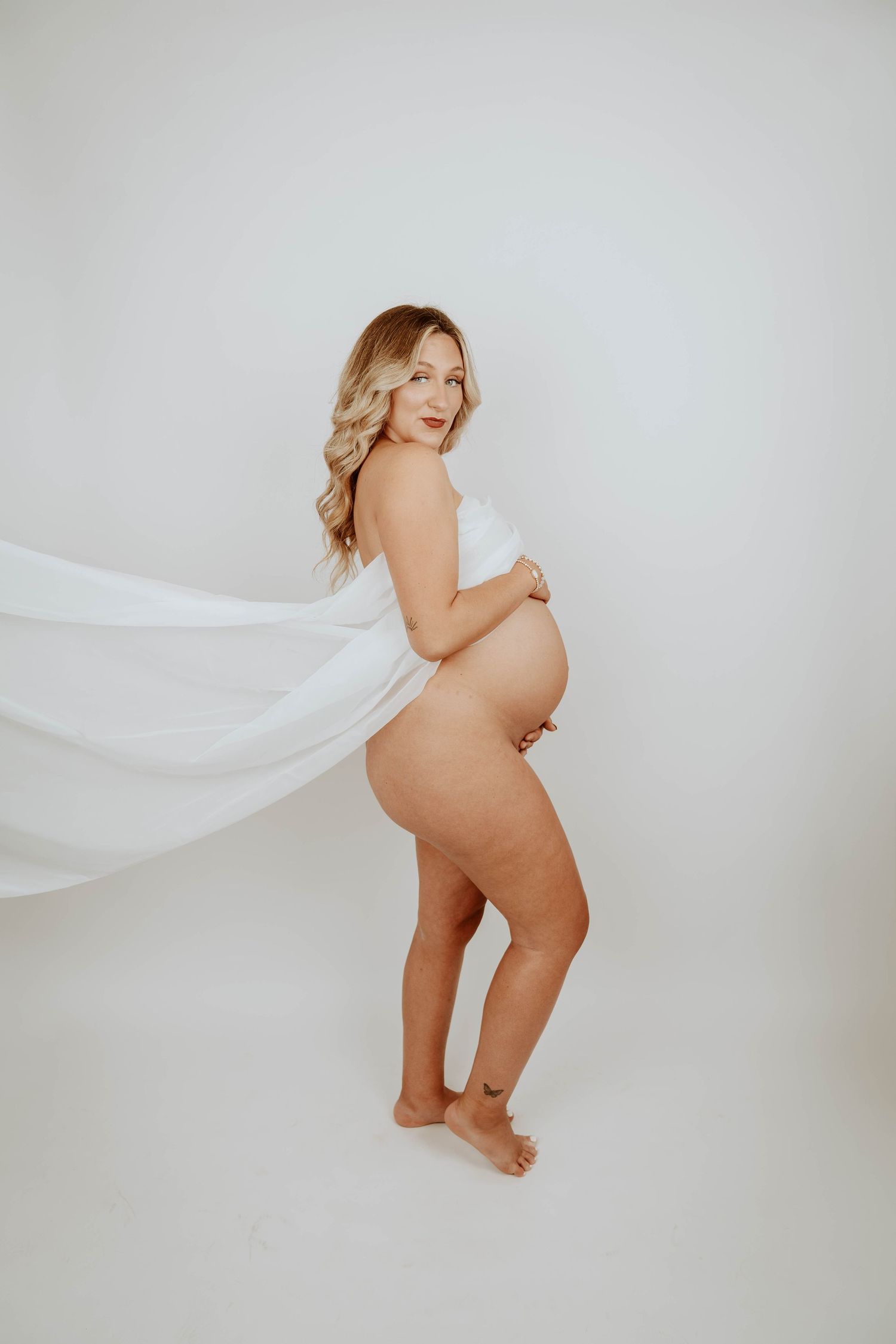 A maternity portrait with flowing white fabric in minimalist studio setting.