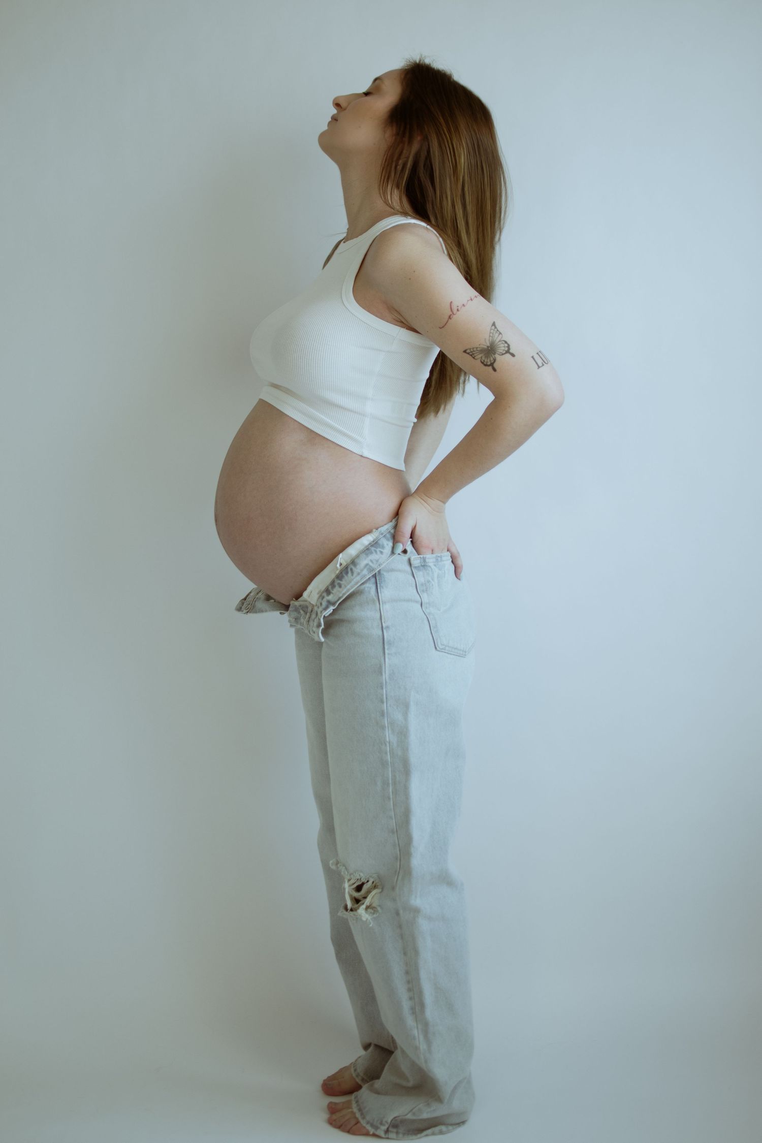 Profile maternity photos showing pregnant belly in light denim and white top.