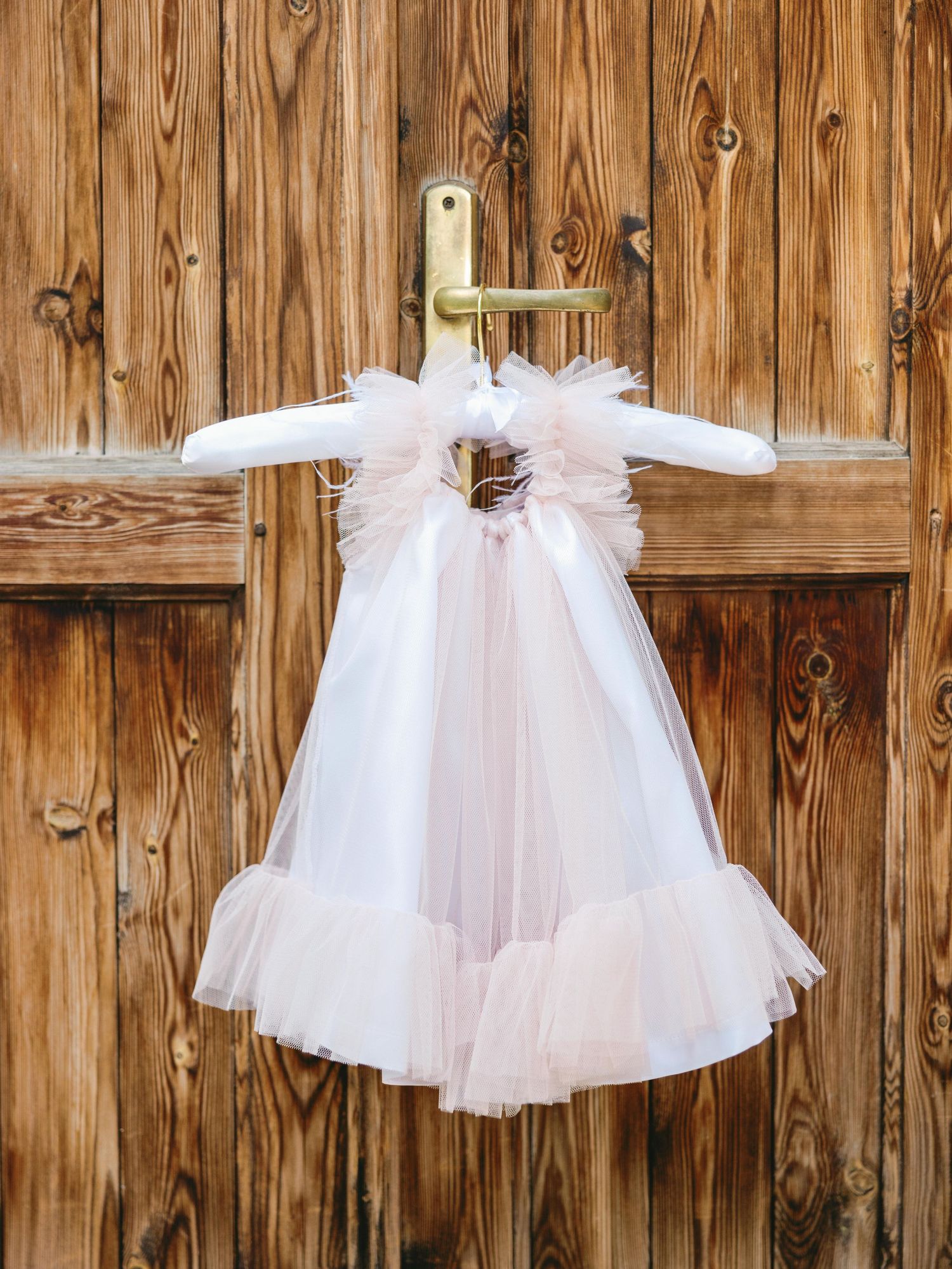 White tulle dresses hanging on a rustic wooden wall create a delicate and ethereal display.