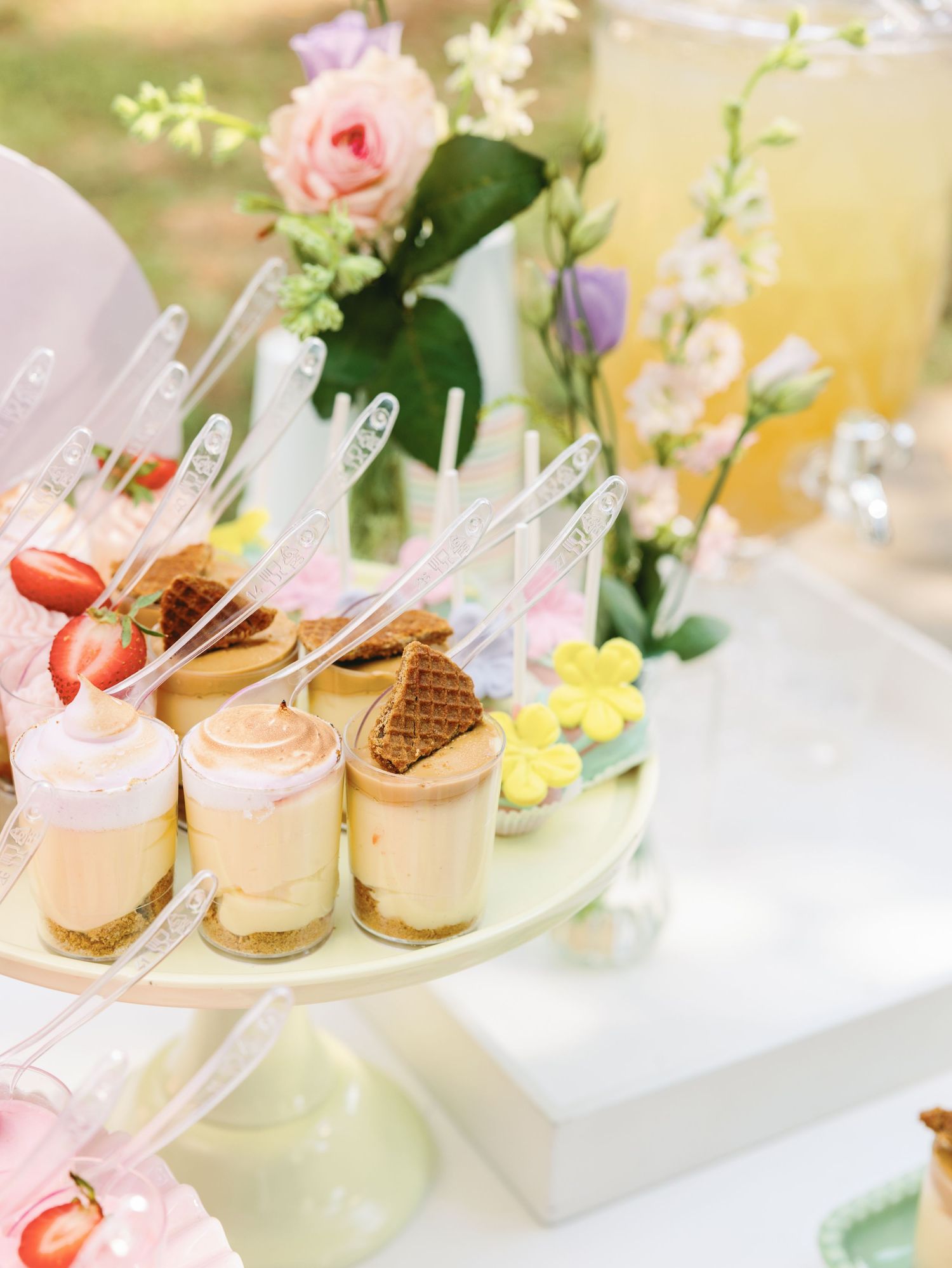 Elegant dessert display featuring mini mousse cups and pink roses on a white table at an upscale event.