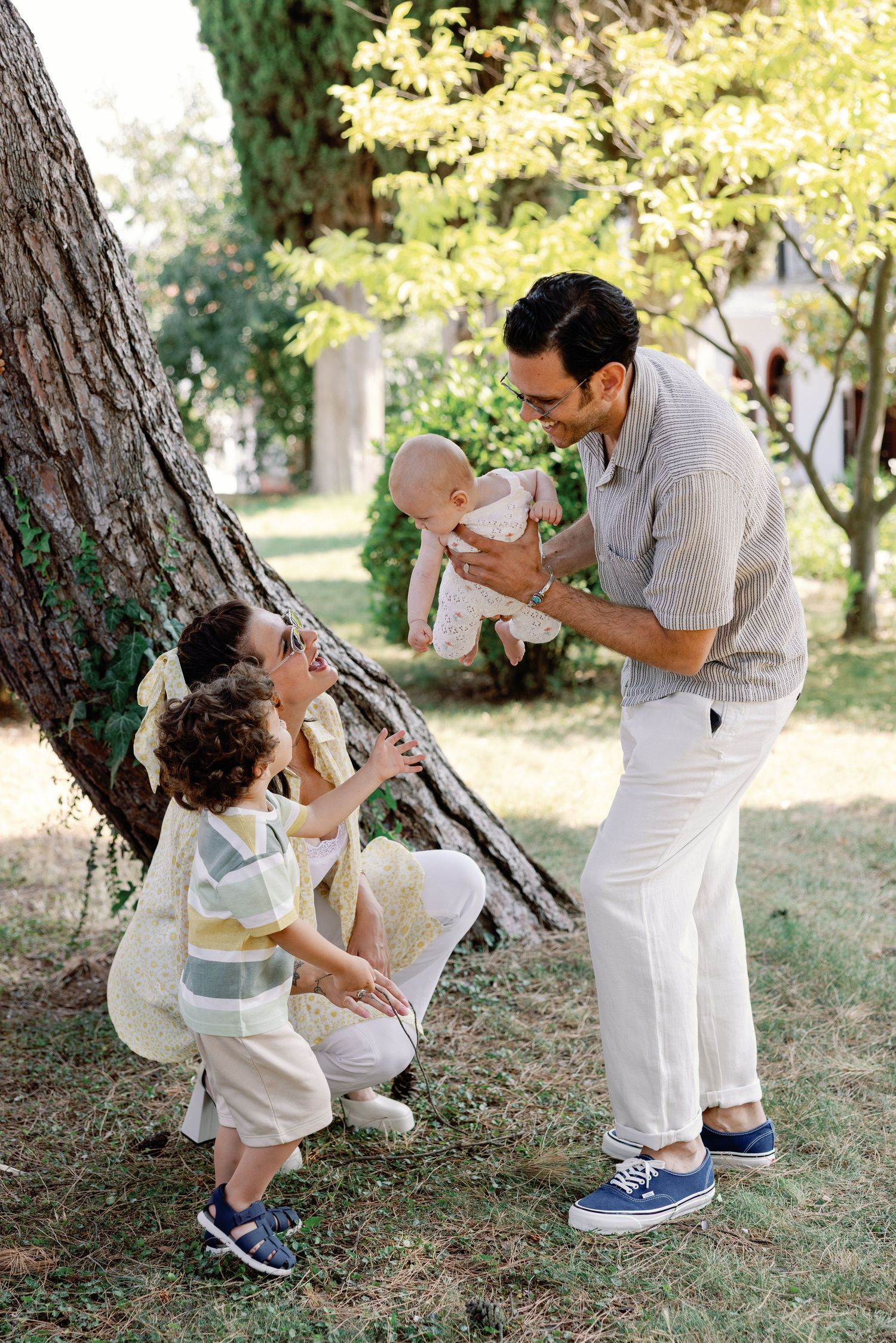 Family sharing a tender moment under a tree in matching white outfits.