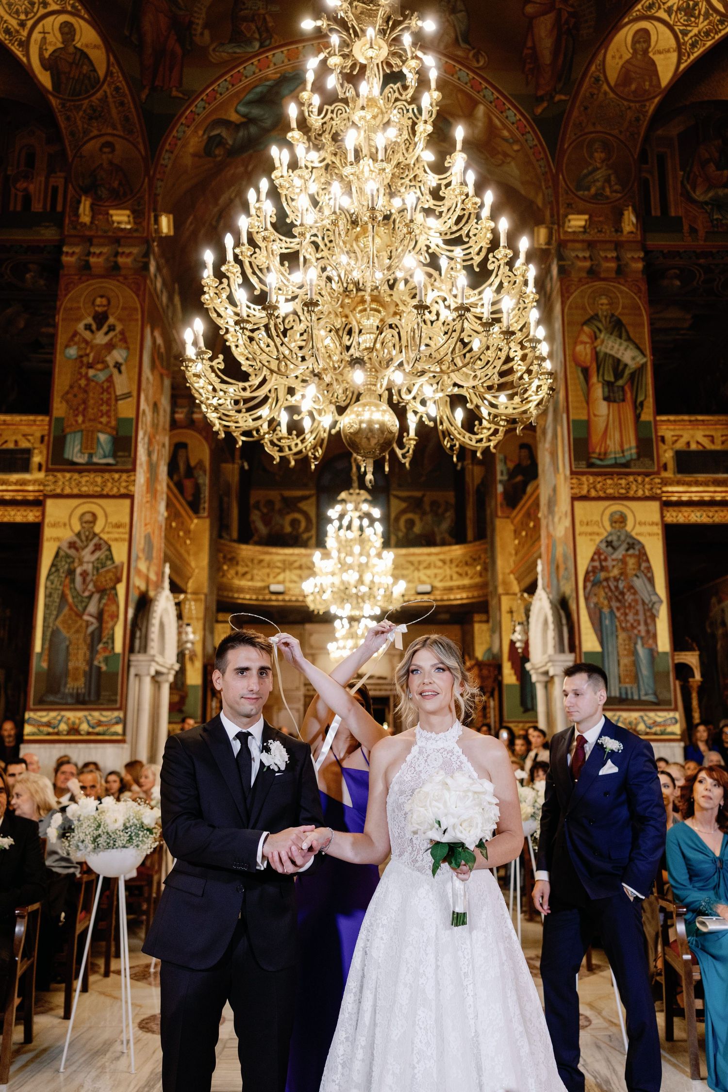 Elegant church ceremony with ornate chandeliers and religious artwork adorning the walls.