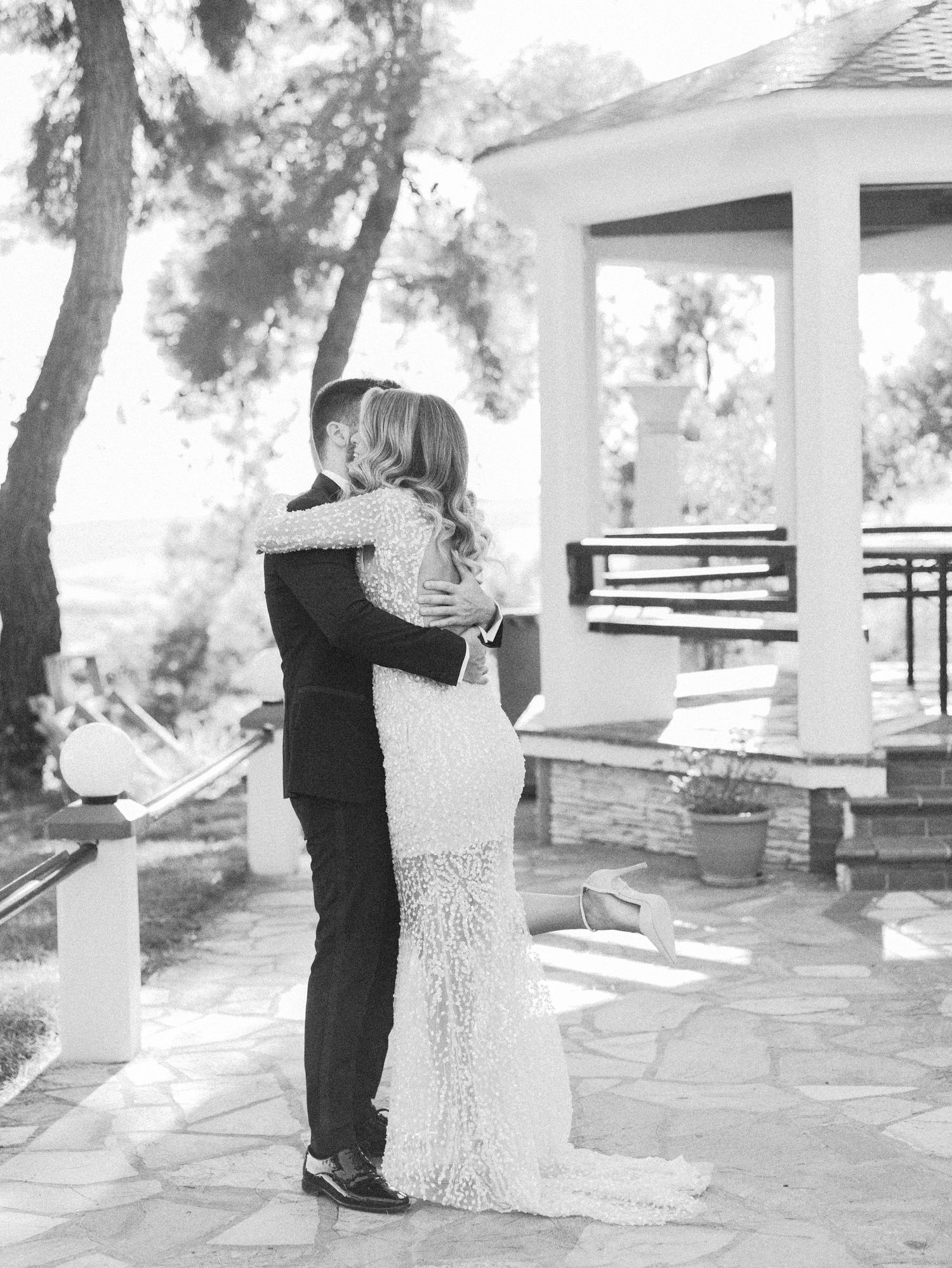 Romantic wedding couple embraces in a series of candid moments on a stone patio surrounded by trees.