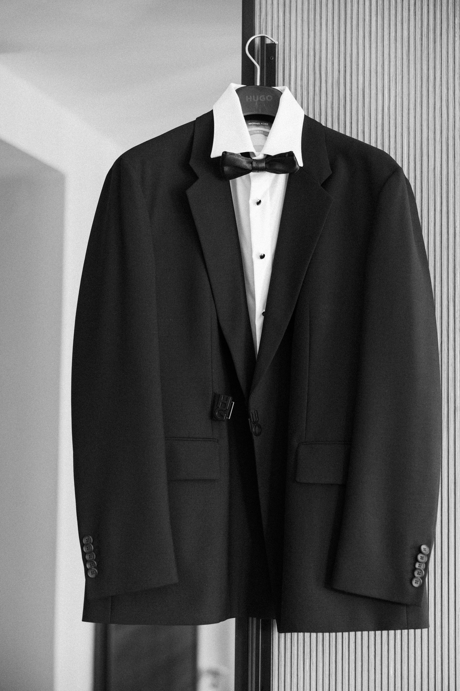 Classic black tuxedo jacket with white dress shirt and bow tie hanging on display.