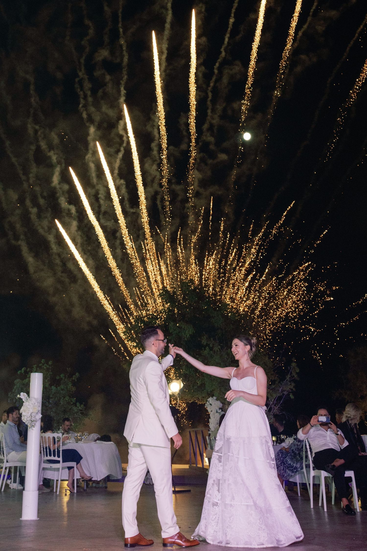Couple dancing under spectacular golden fireworks display at outdoor wedding reception.