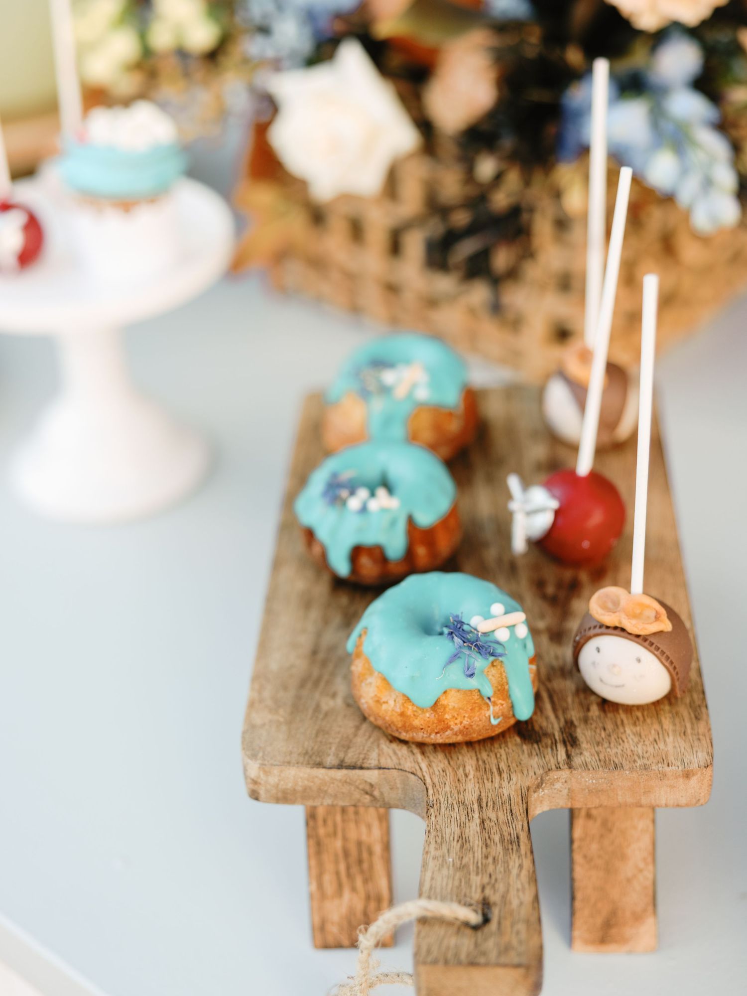 Turquoise glazed mini donuts and candy apples displayed on a rustic wooden serving board at a dessert table.