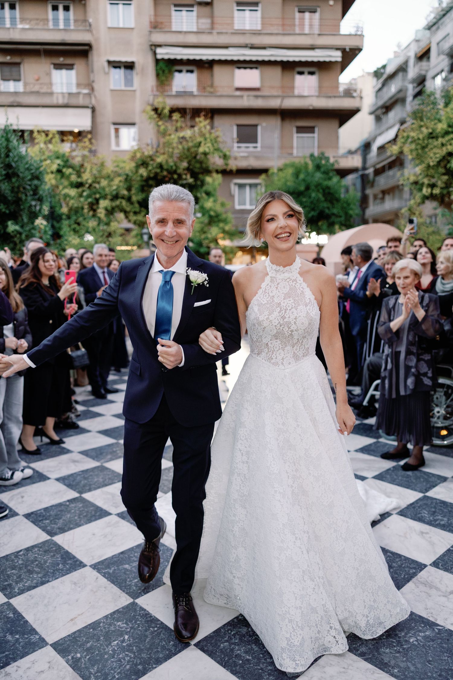Wedding celebration on checkered floor with guests cheering in background.