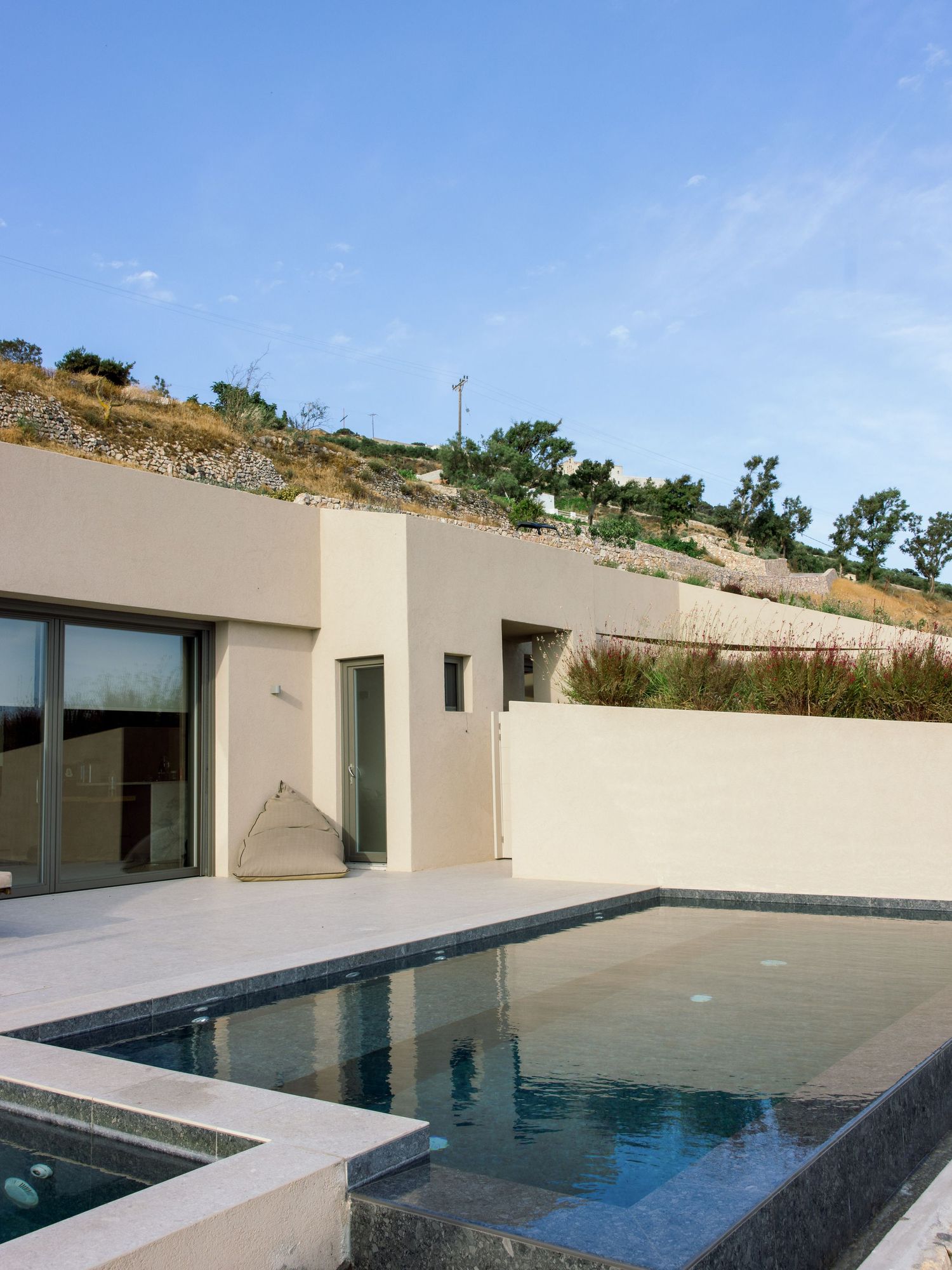 Modern hillside villa with infinity pool and clean architectural lines against blue sky.