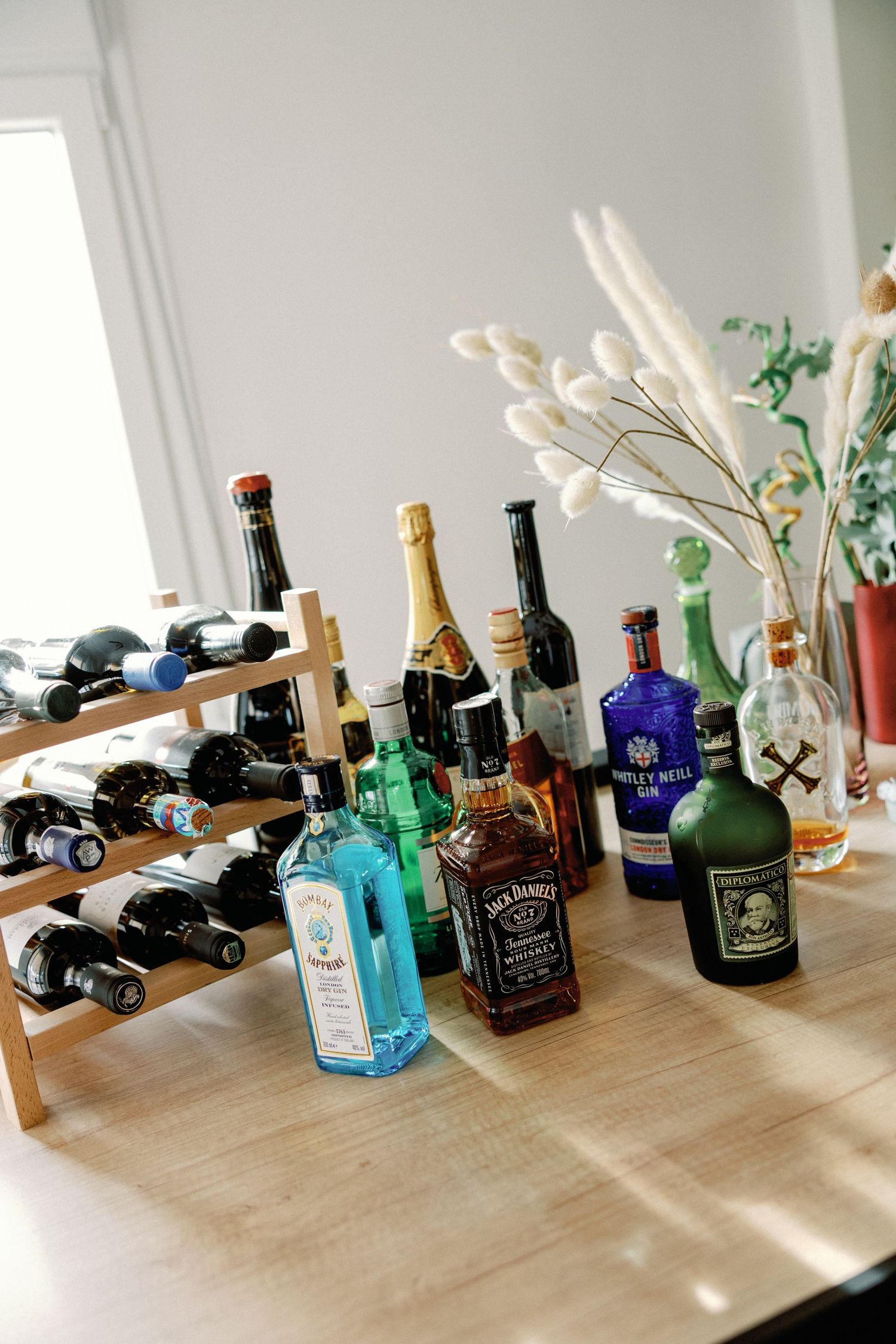 Collection of liquor bottles and decorative dried flowers arranged on wooden surface.