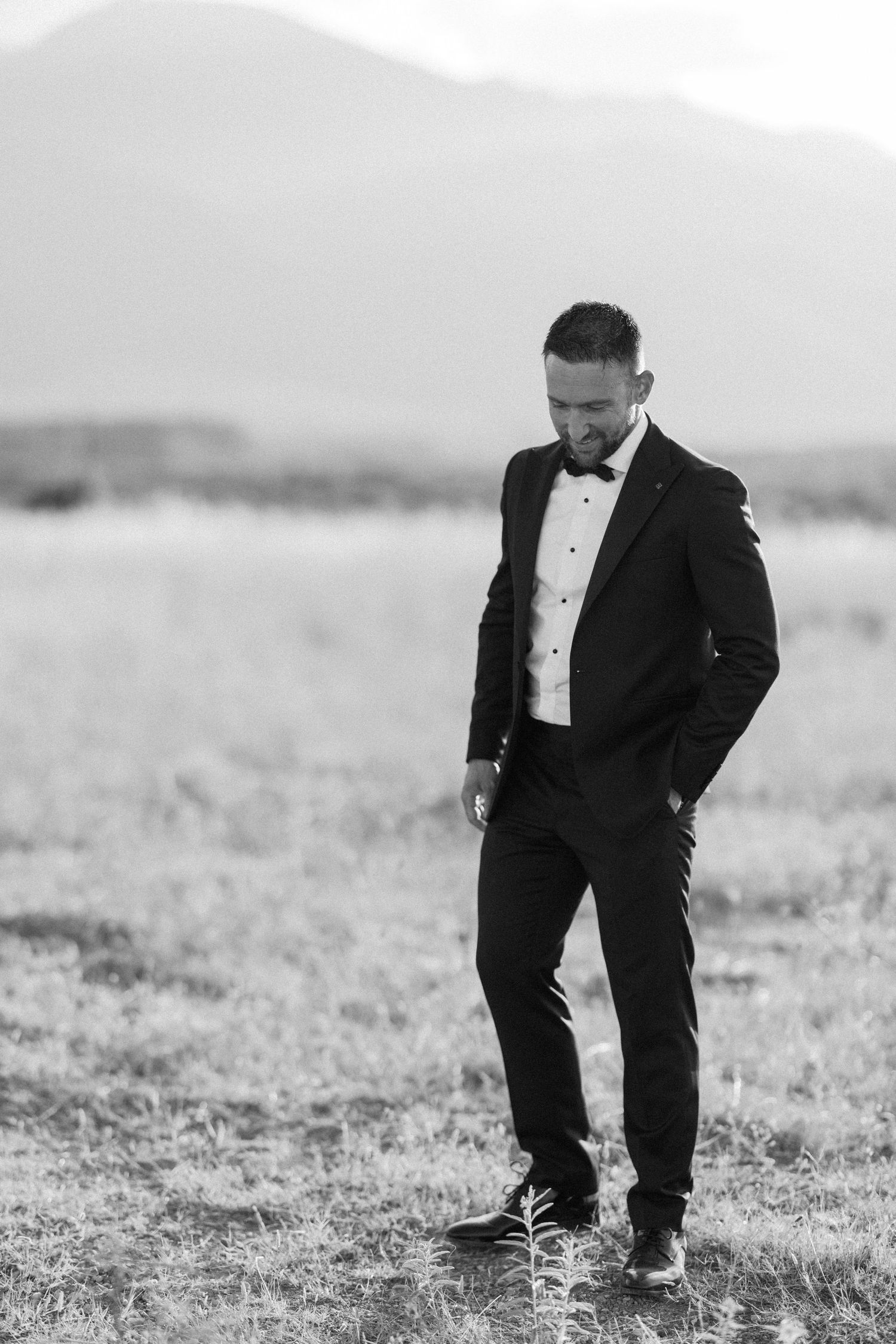 A person in formal attire walks through a misty field in black and white.