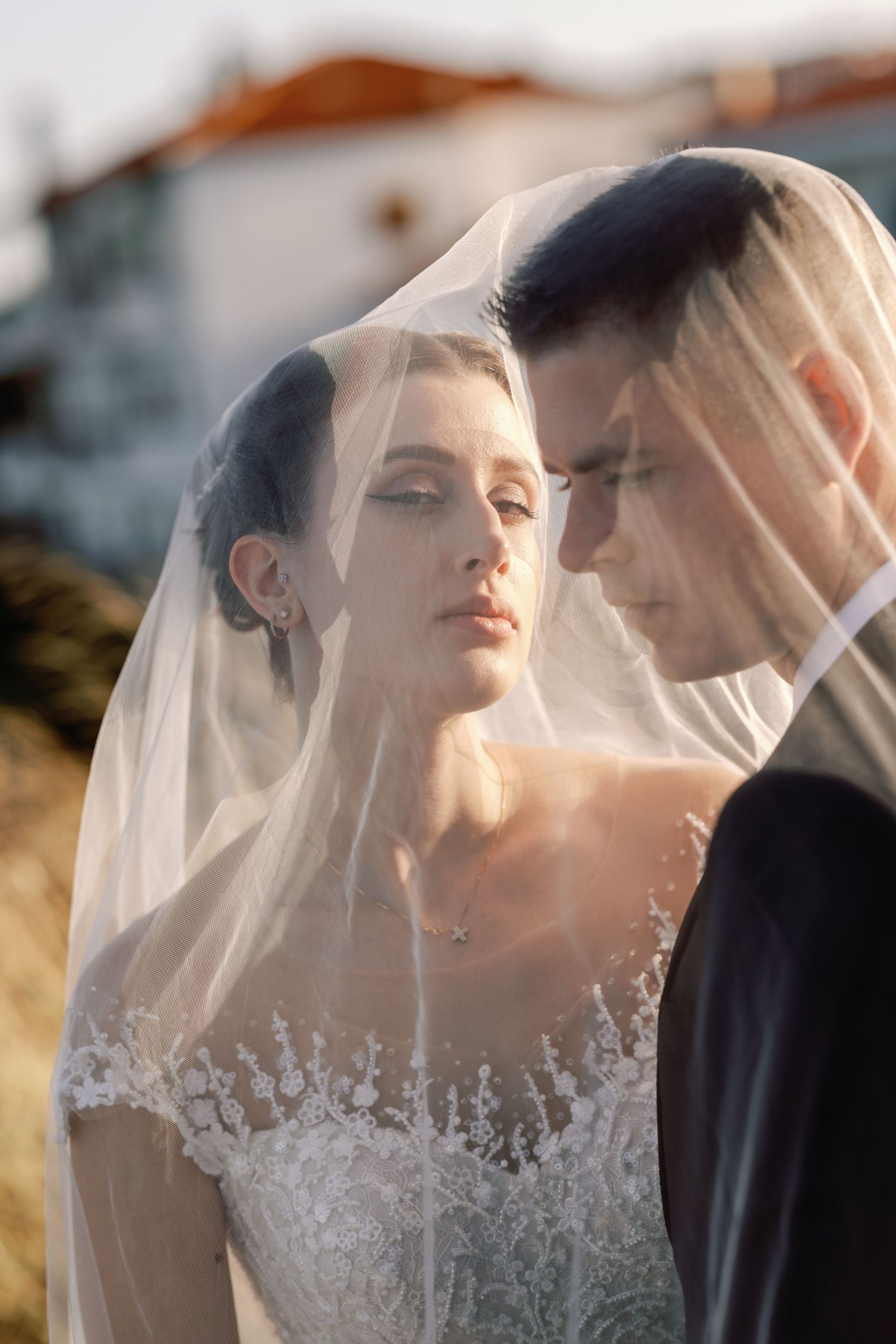 Romantic sunset portraits of wedding couple under sheer veil in golden light.