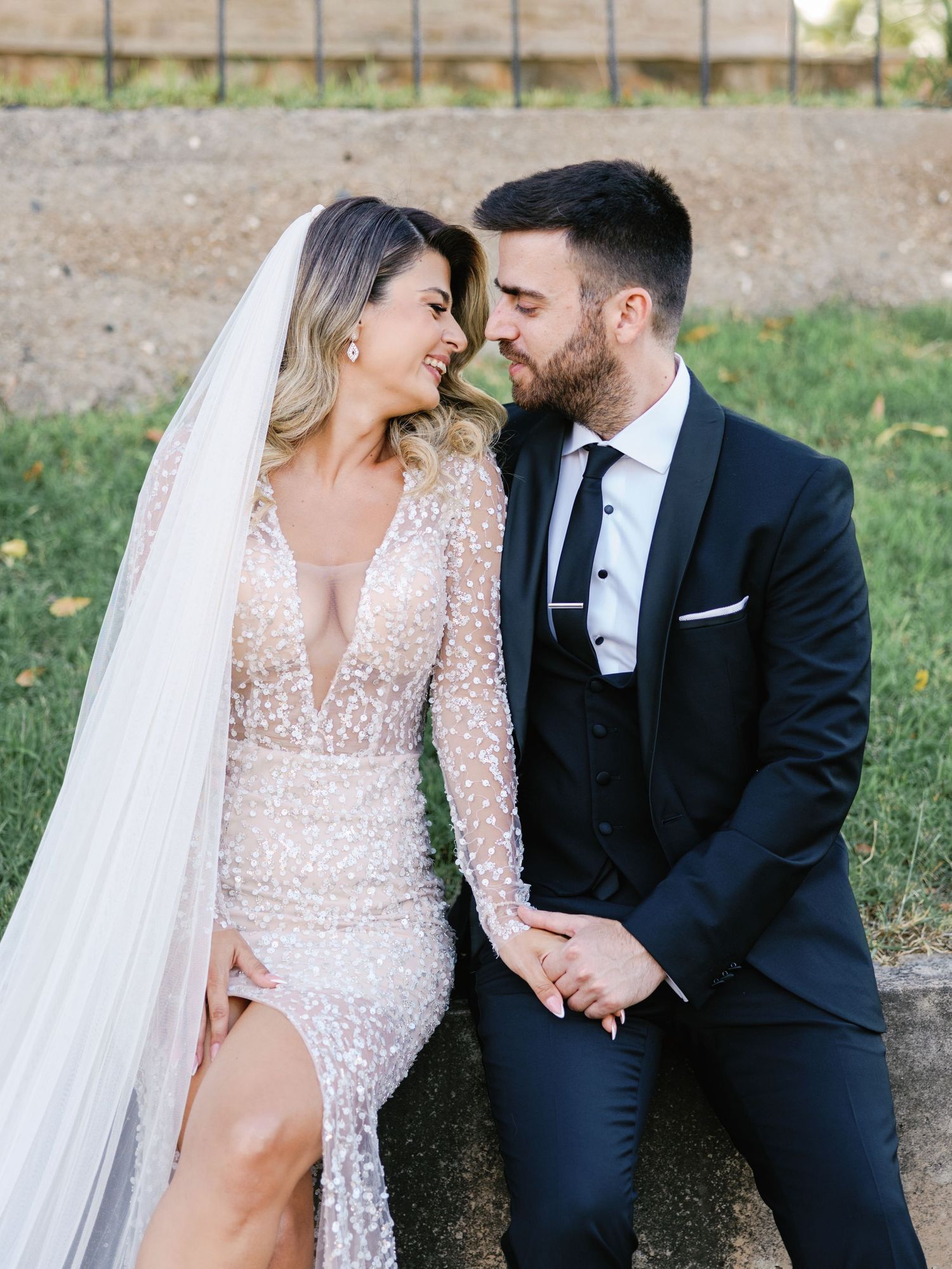 Wedding couple shares intimate moments on rustic garden bench during outdoor photoshoot.