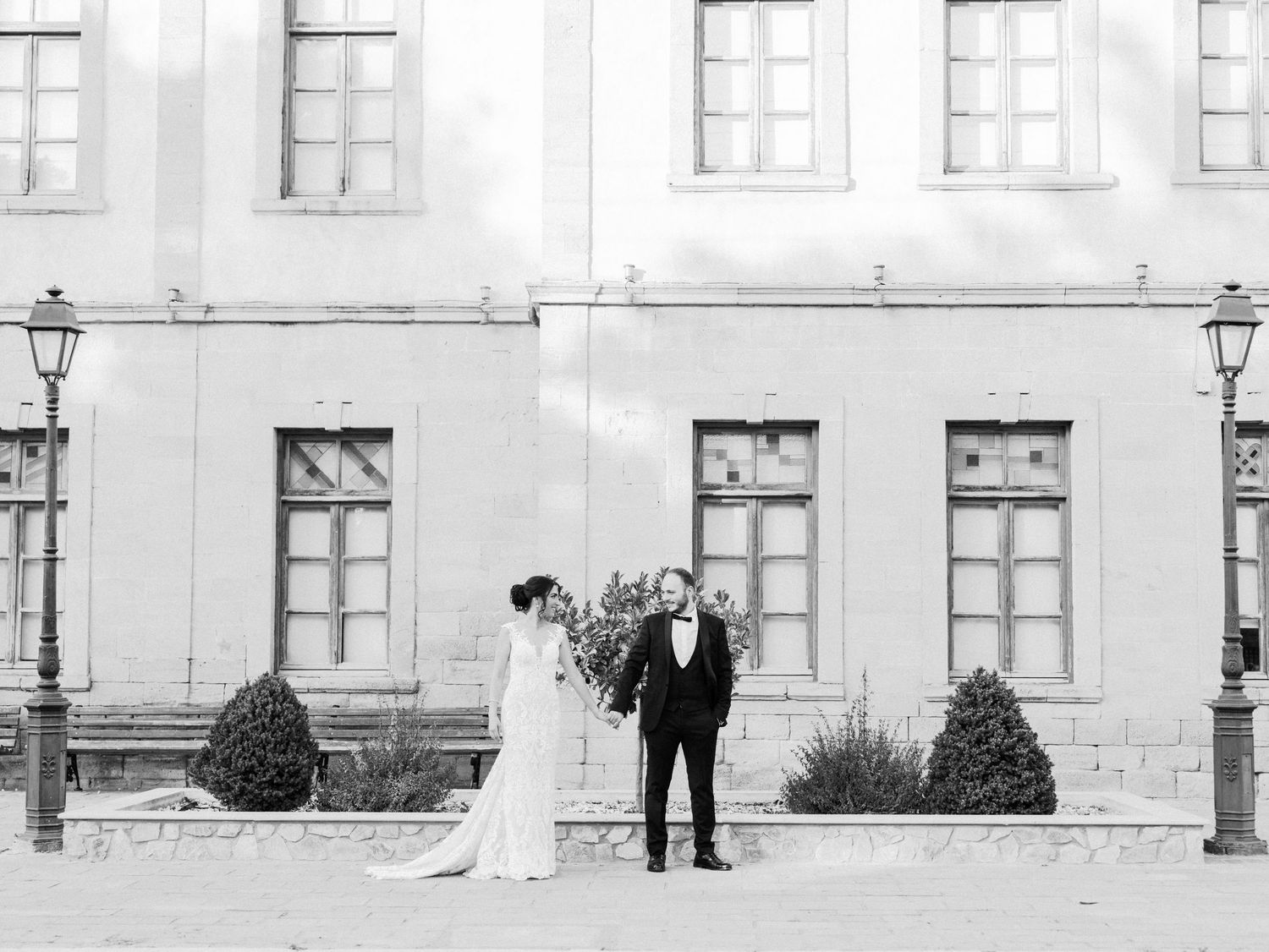 Black and white wedding portrait against classic architecture with multiple windows.