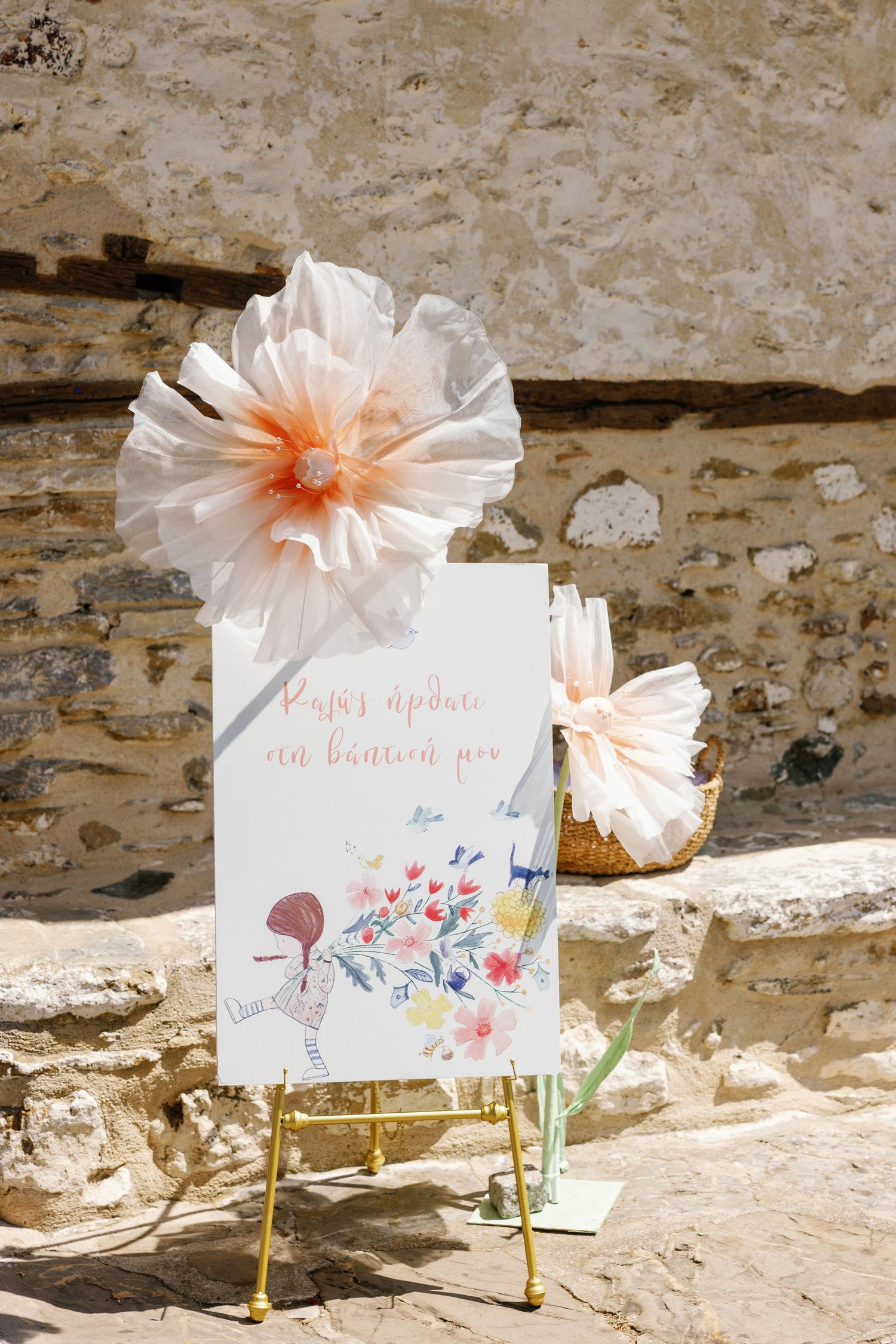 Delicate paper flowers and watercolor signs displayed against a rustic stone wall.