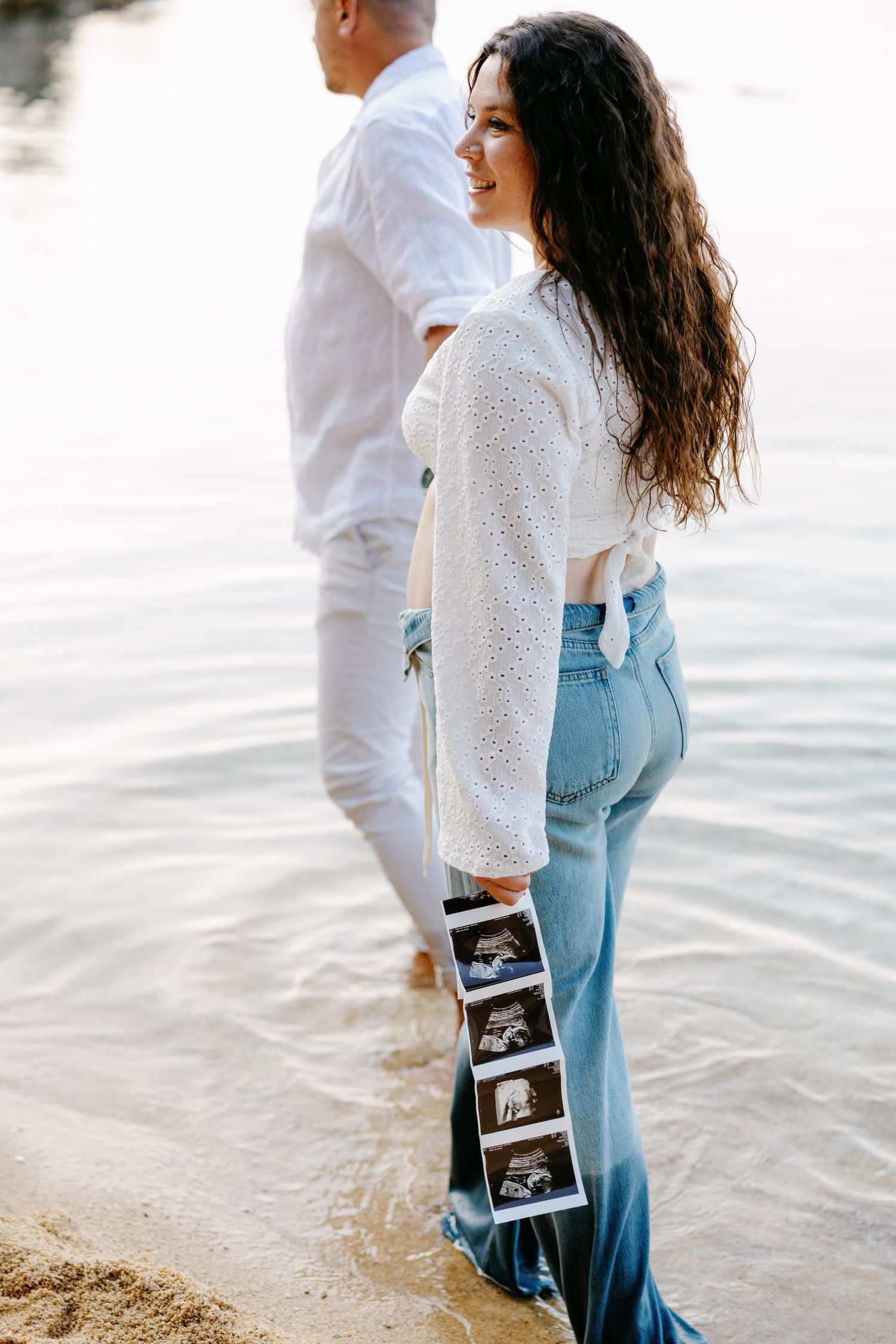 Maternity beach photos with couple displaying ultrasound images by the water.