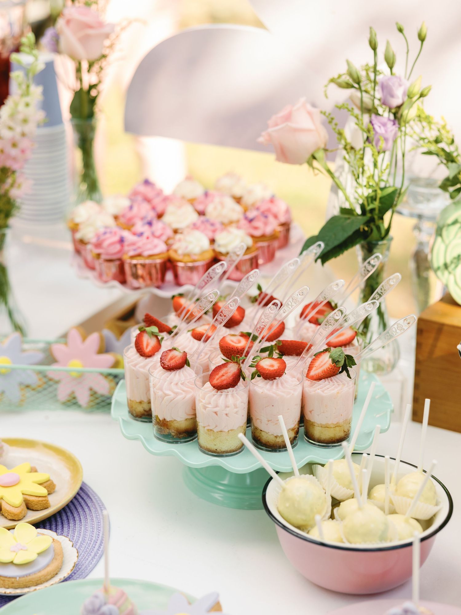 Elegant dessert table with pink macarons, strawberry cakes, and pastel treats arranged on mint green cake stands.