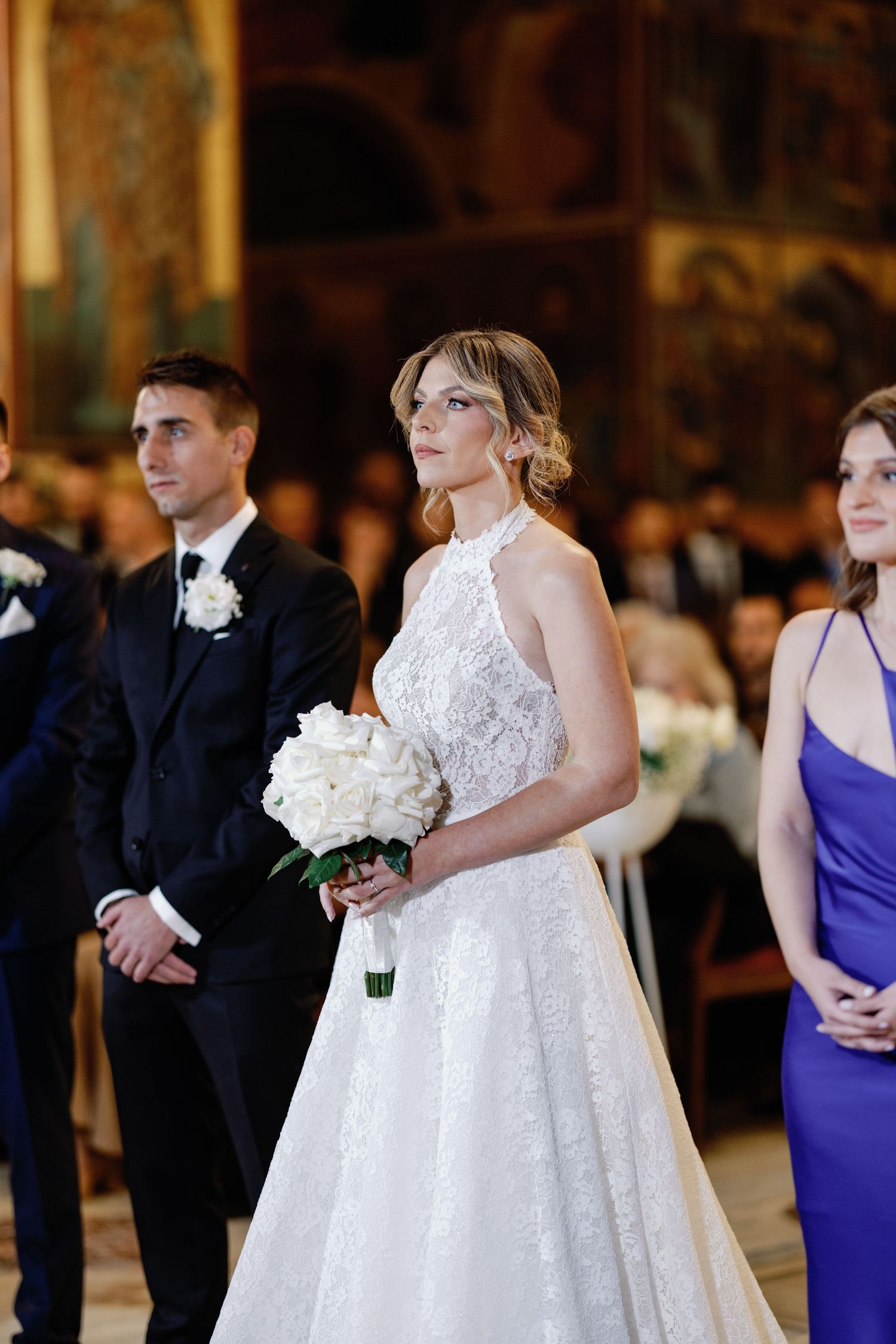 Wedding ceremony in an ornate venue with guests watching couple in elegant attire.