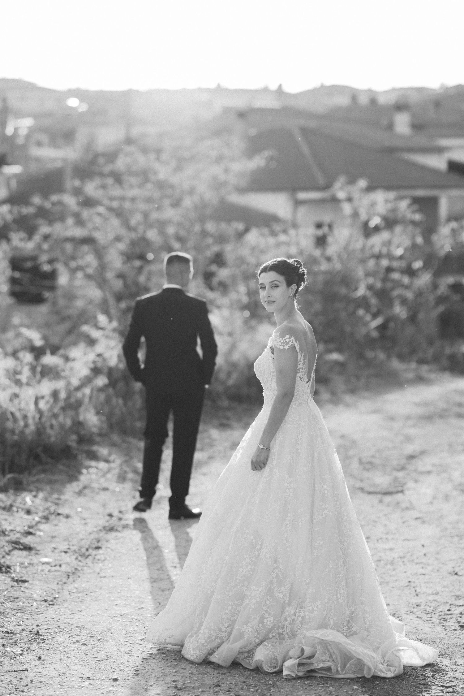 Wedding dress silhouette follows bride walking along rustic outdoor path in black and white.