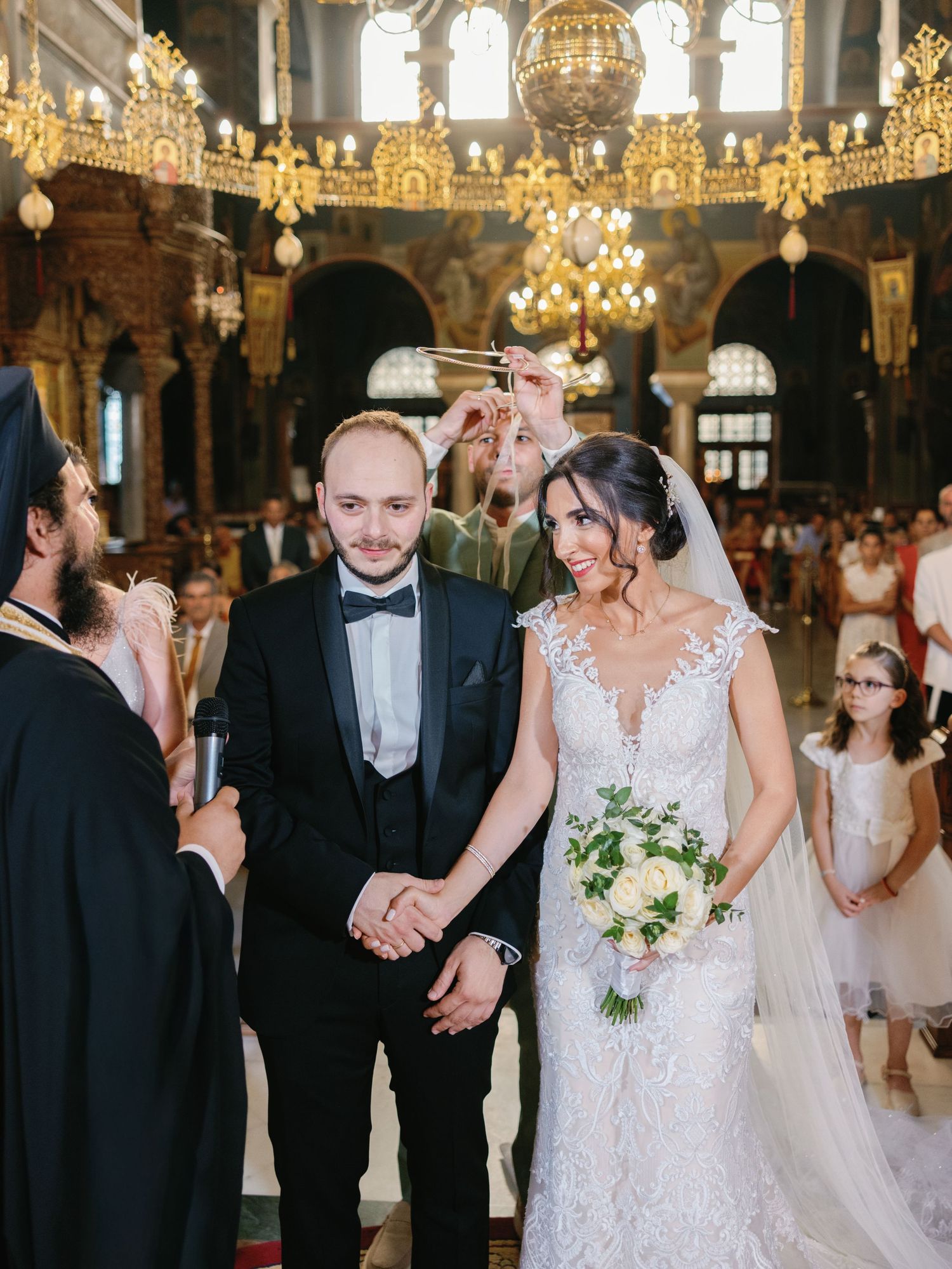 A wedding ceremony in an ornate Orthodox church with golden chandeliers and decorative details.