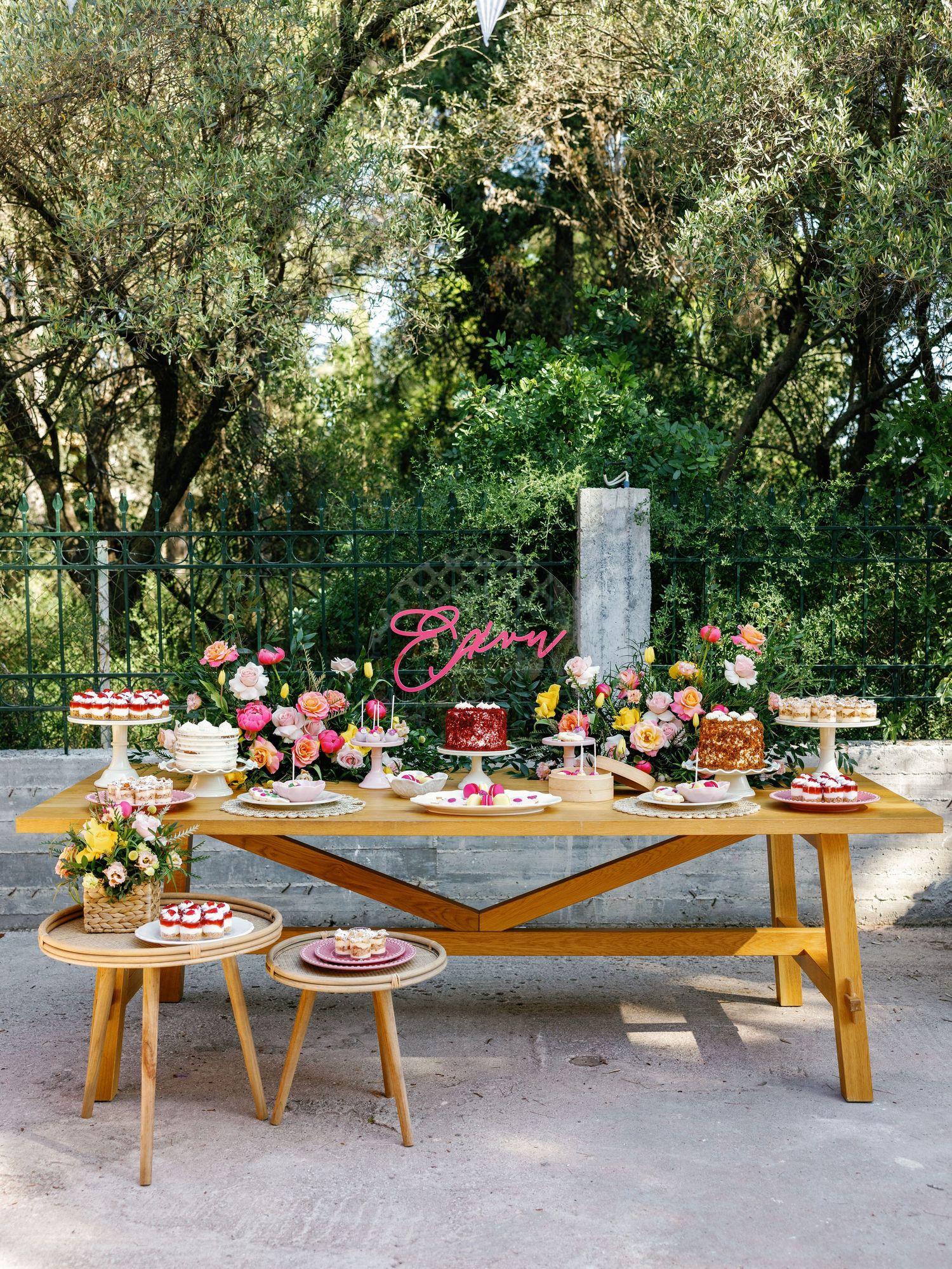 Rustic wooden dessert display tables decorated with colorful flowers and sweet treats at an outdoor garden party setting.