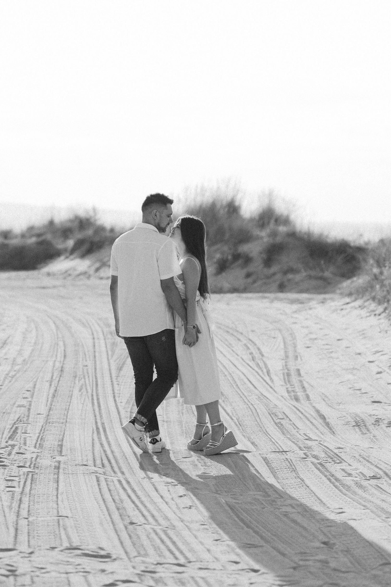 Black and white photo of couple walking together on sandy path.