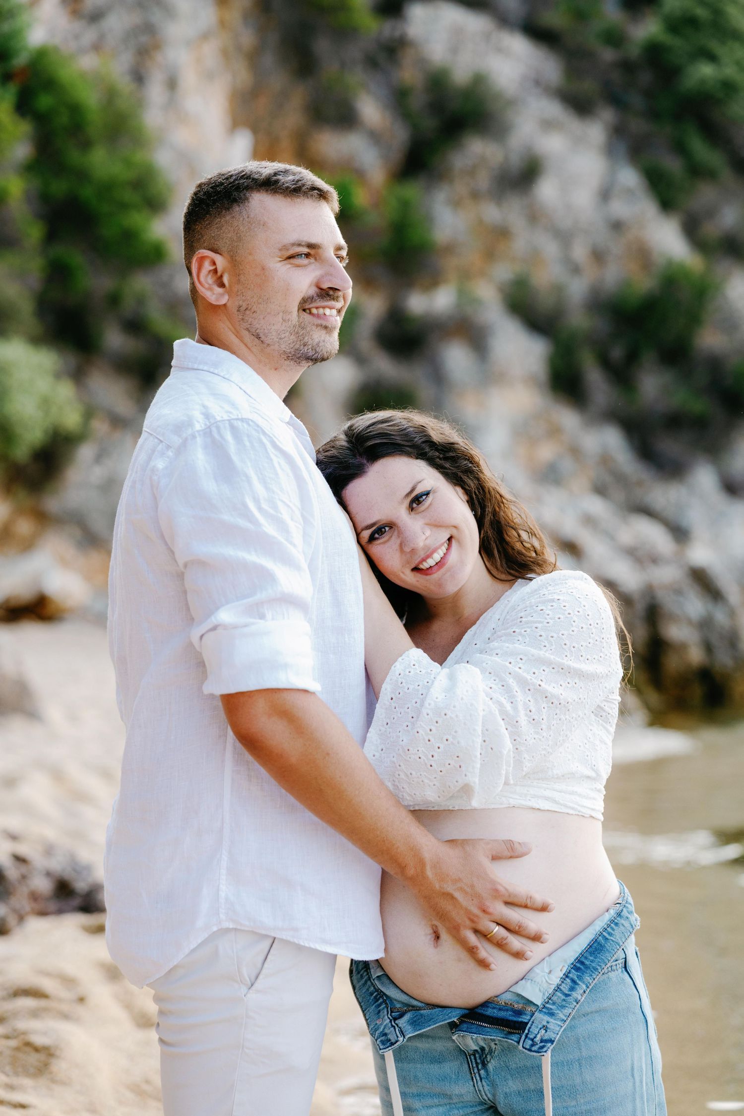 Couple embraces on a scenic beach with rocky cliffs in the background during a romantic photoshoot.