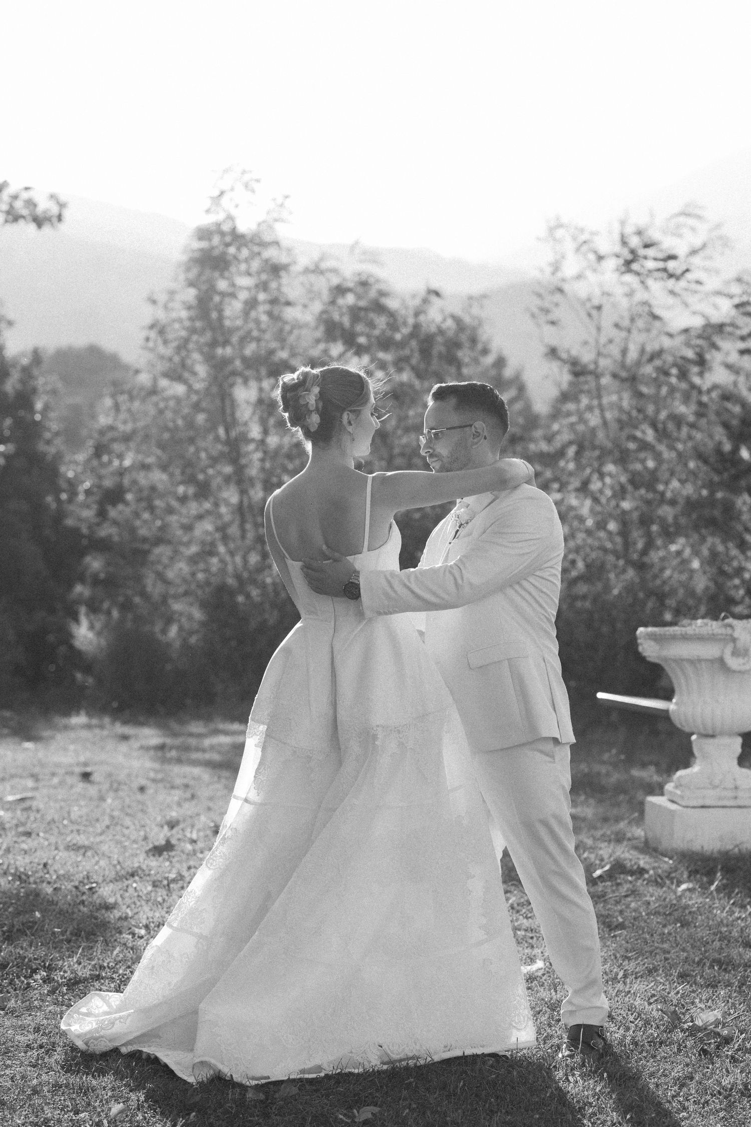 A romantic wedding couple dances together outdoors with mountains and trees in the background.