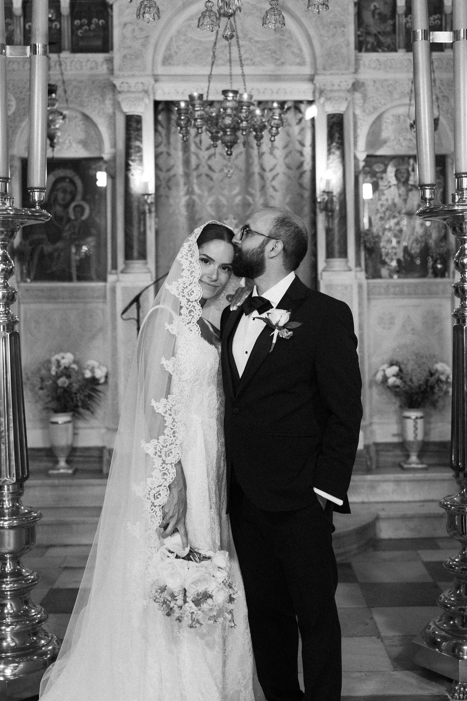 Black and white photo of a bride and groom sharing a tender moment inside an ornate church on their wedding day.