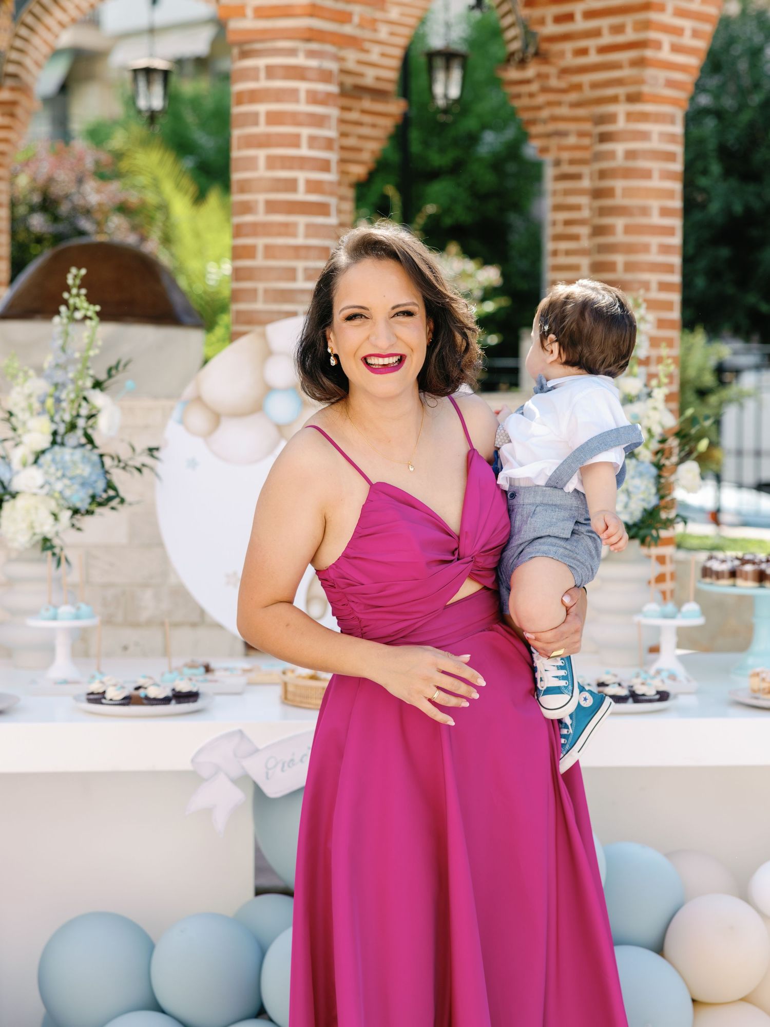 A person in a magenta bridesmaid dress poses outdoors near brick columns during a wedding celebration.
