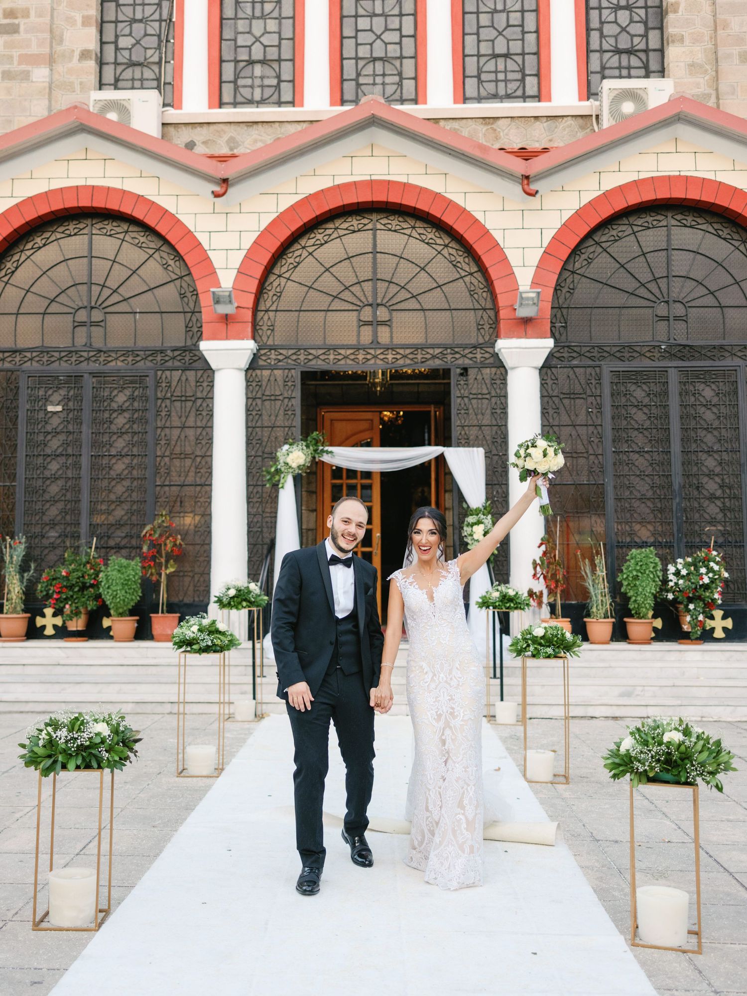A wedding couple walks outside a beautiful stone church with arched windows and decorative architecture.