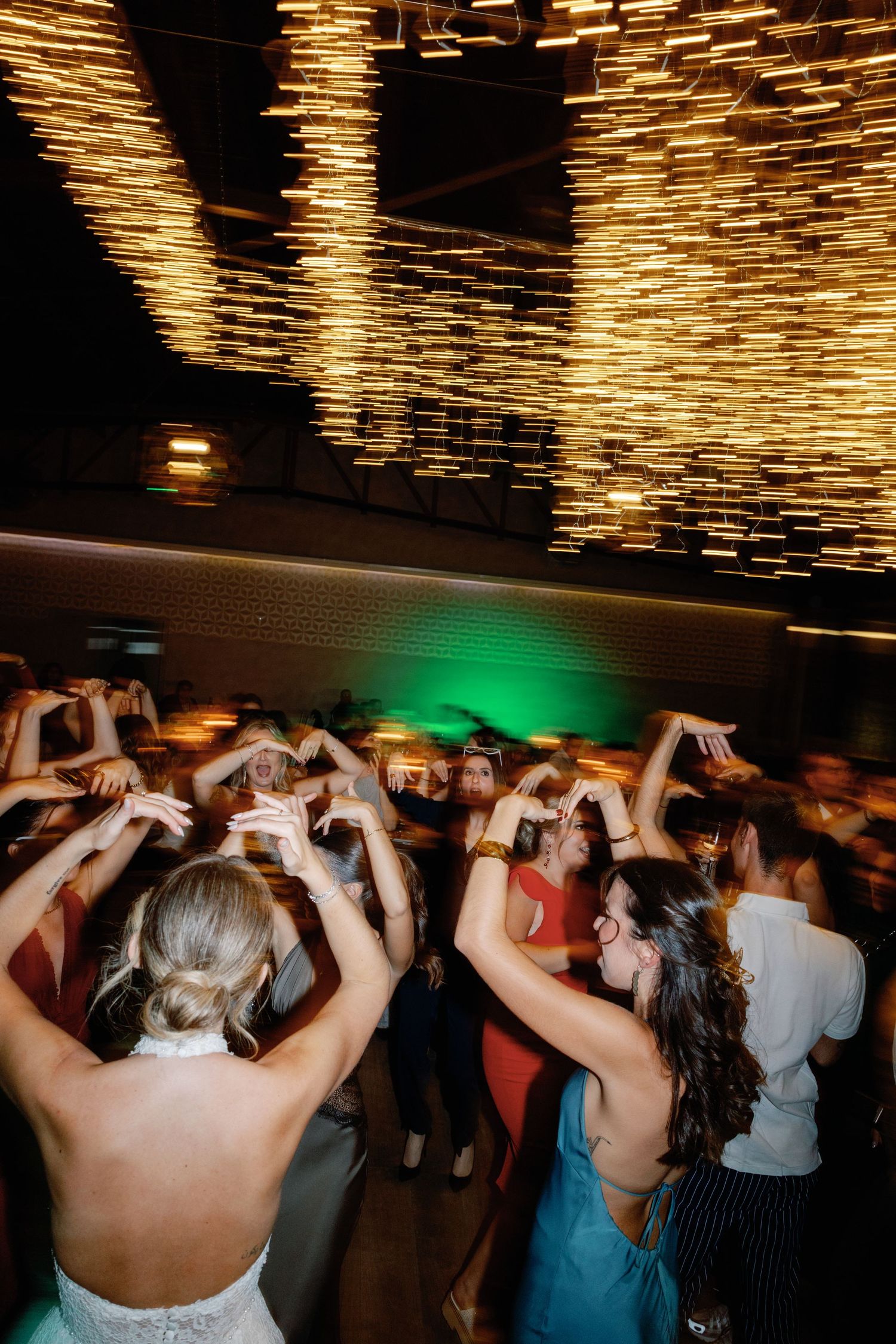 Wedding guests dancing beneath a dramatic golden light installation.