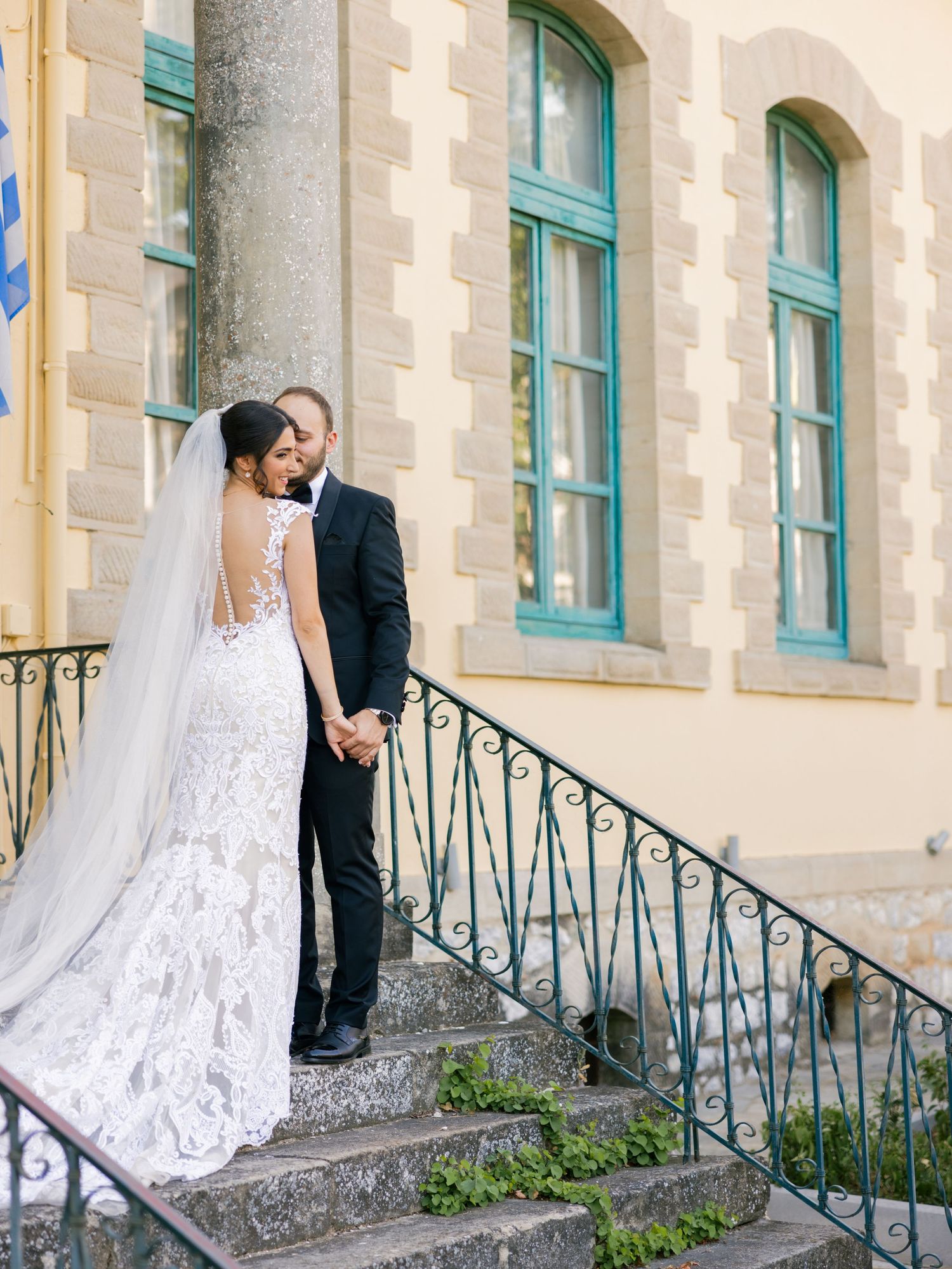 Elegant wedding couple posing on stone steps with ornate iron railing at historic building.