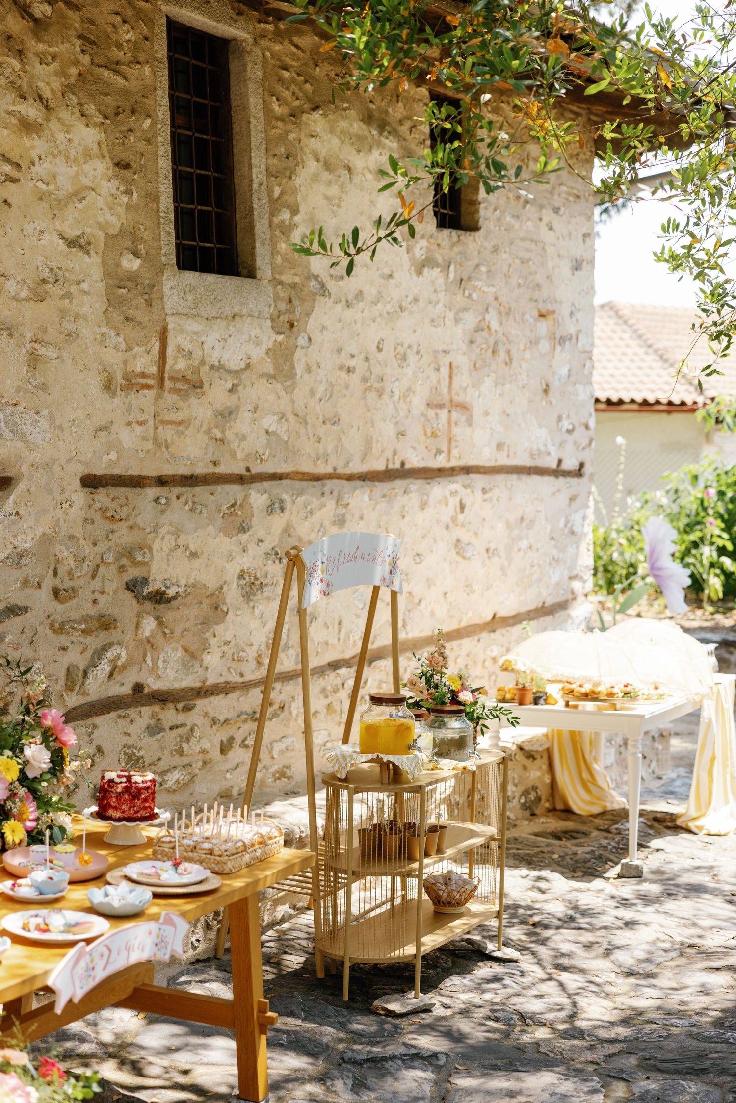 Outdoor dining setup against rustic stone wall with wooden tables and floral decorations.