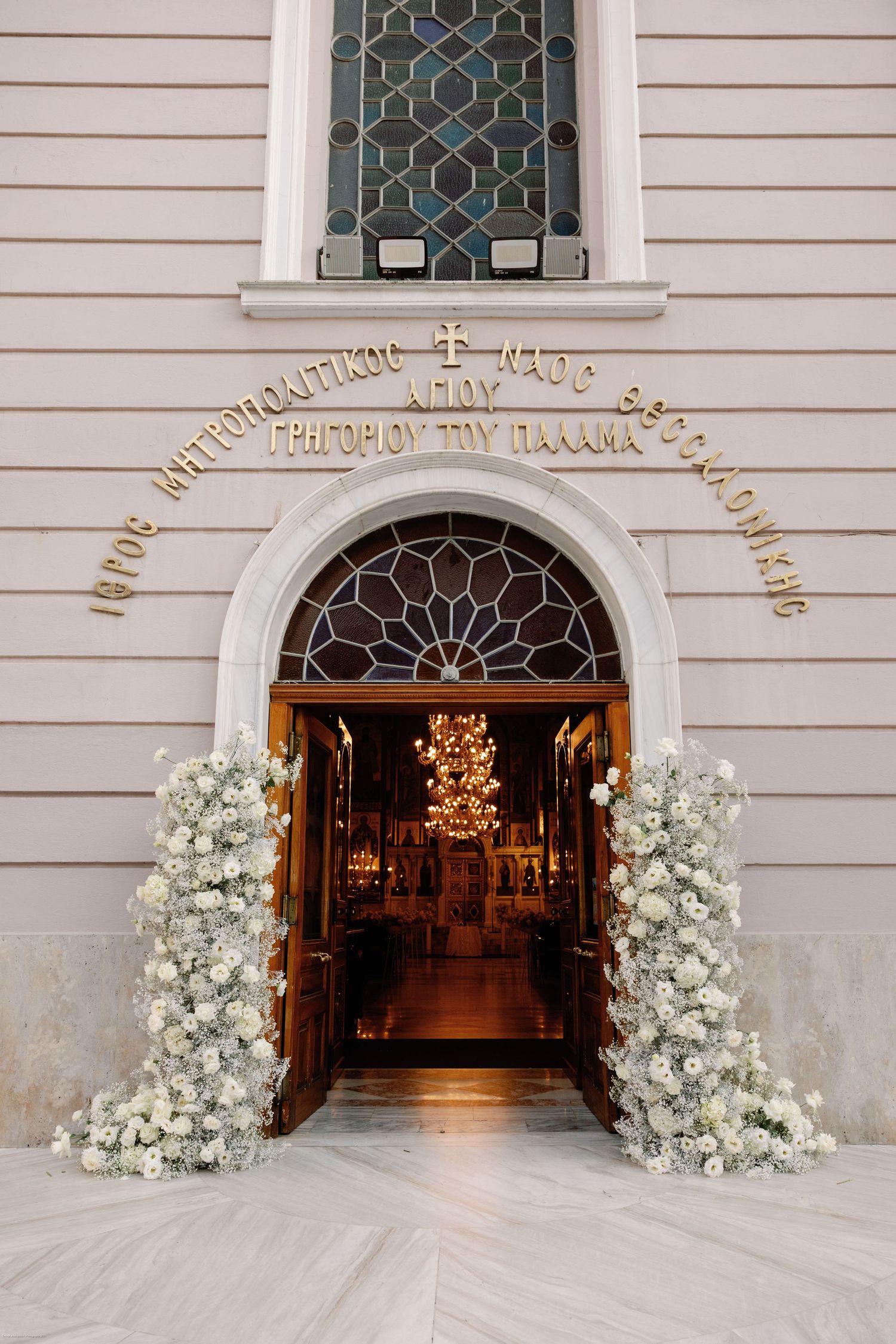 Church entrance decorated with white floral arrangements and illuminated archway for wedding ceremony.