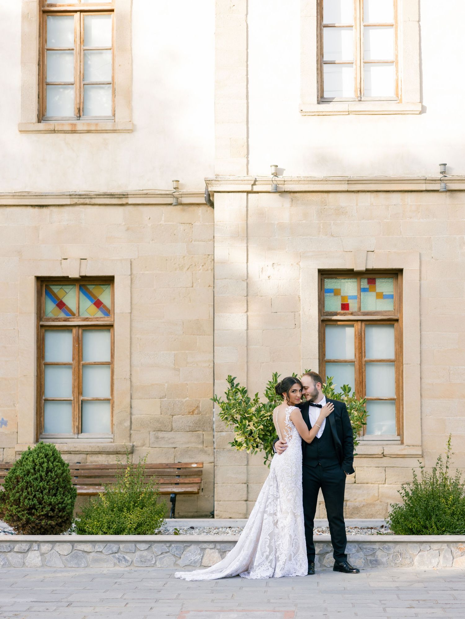 Wedding couple embracing outside historic stone building with traditional windows.