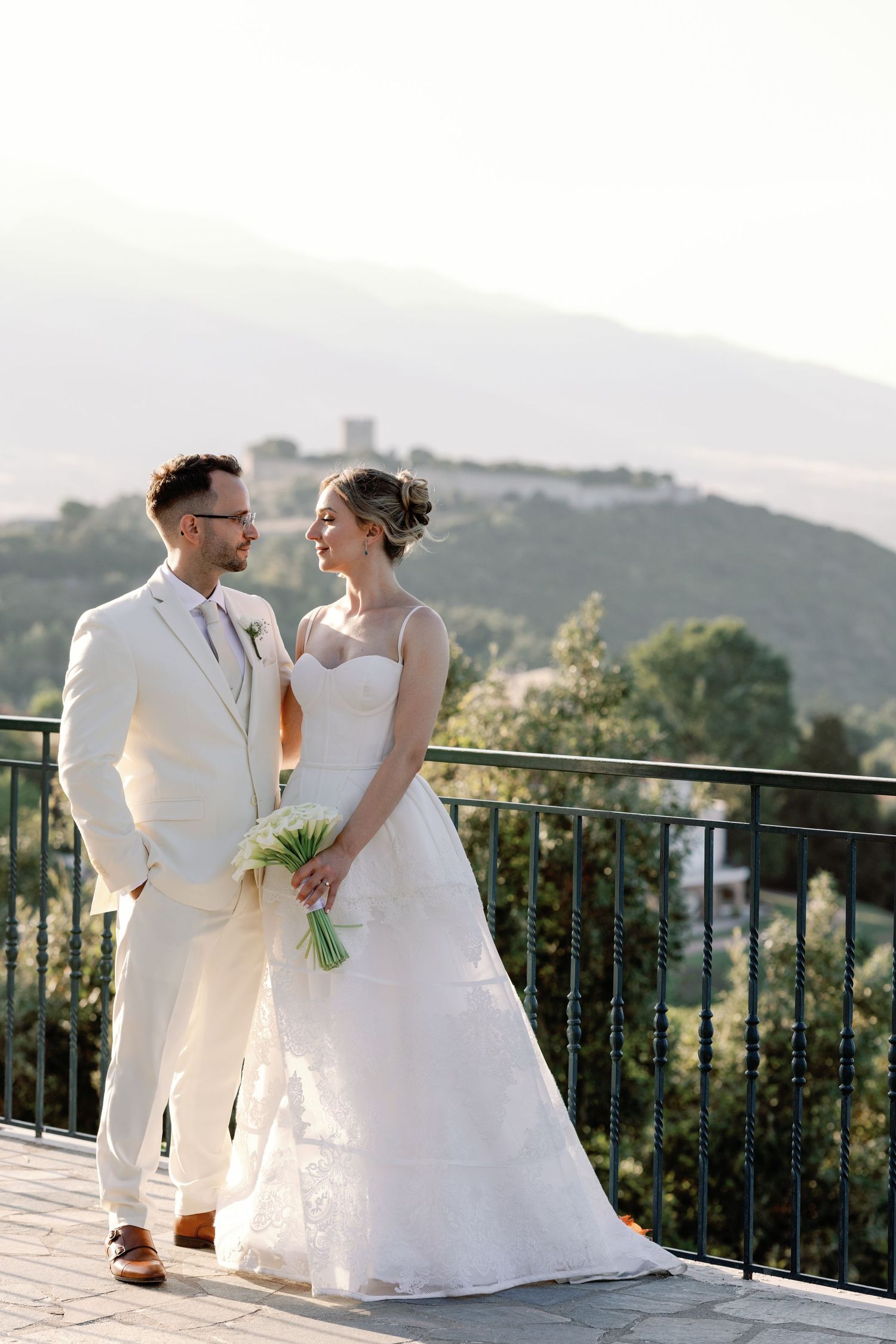 Wedding couple sharing intimate moment on terrace overlooking mountain landscape.