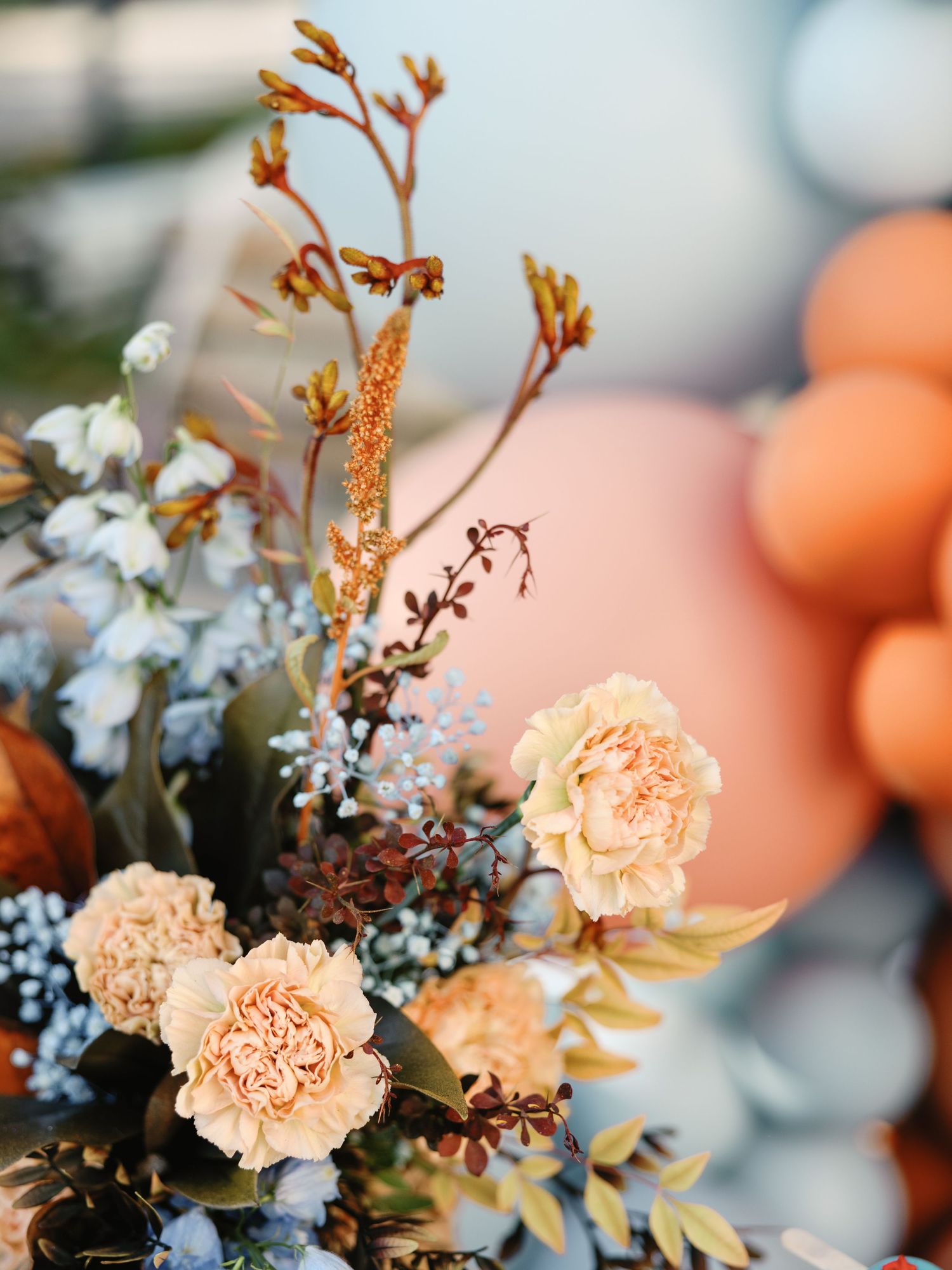 Delicate peach carnations and white flowers arranged with dried foliage in a soft, romantic wedding bouquet composition.