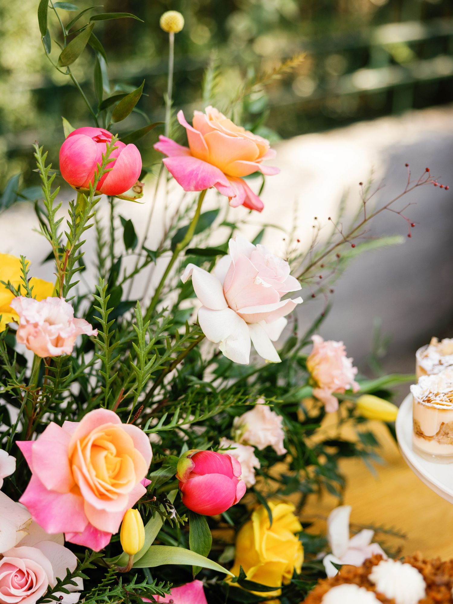 Elegant floral centerpiece featuring pink and yellow roses with greenery arranged on a decorated table setting.