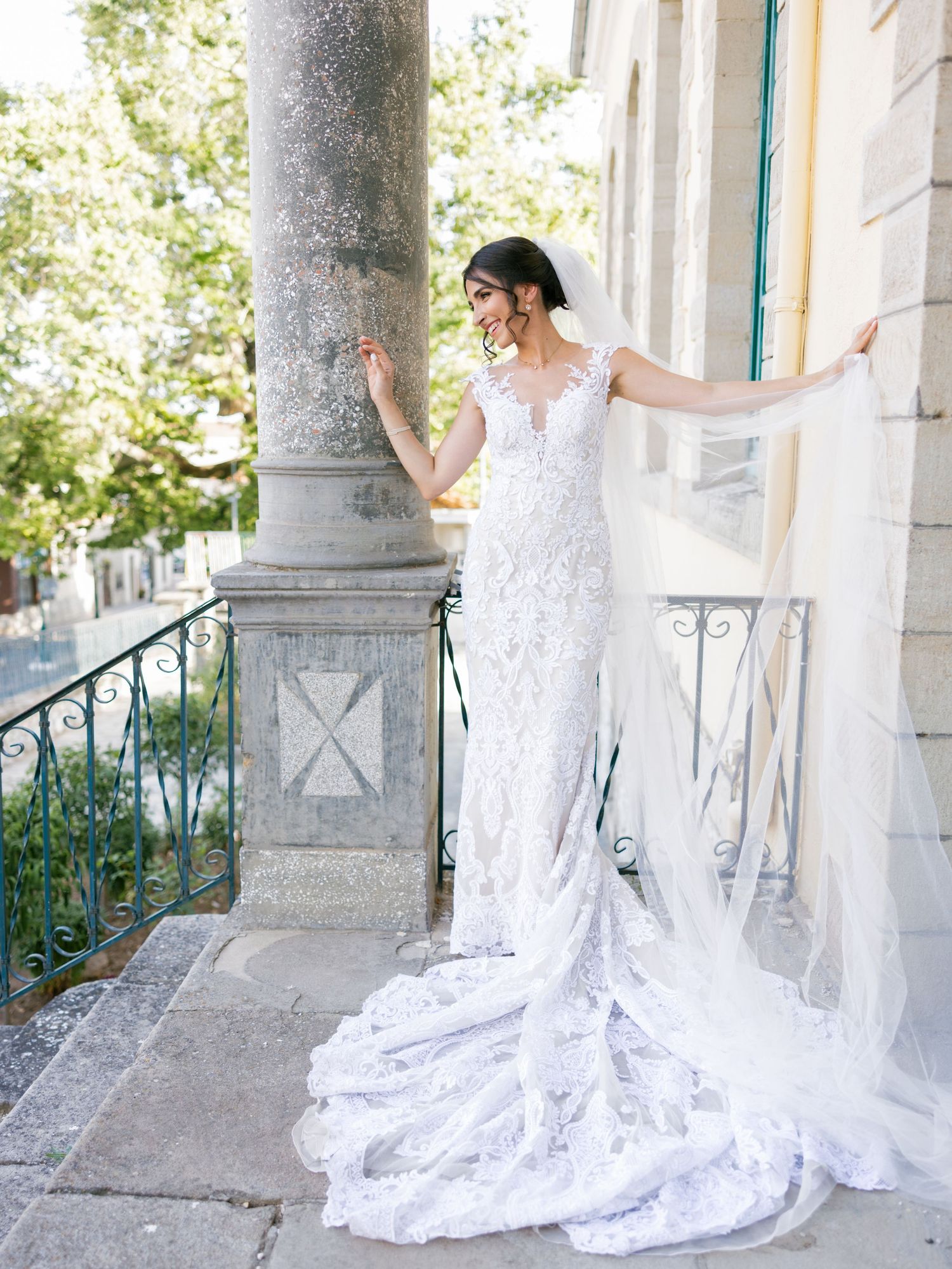 Bride in lace gown with dramatic cathedral train poses against historic building exterior.