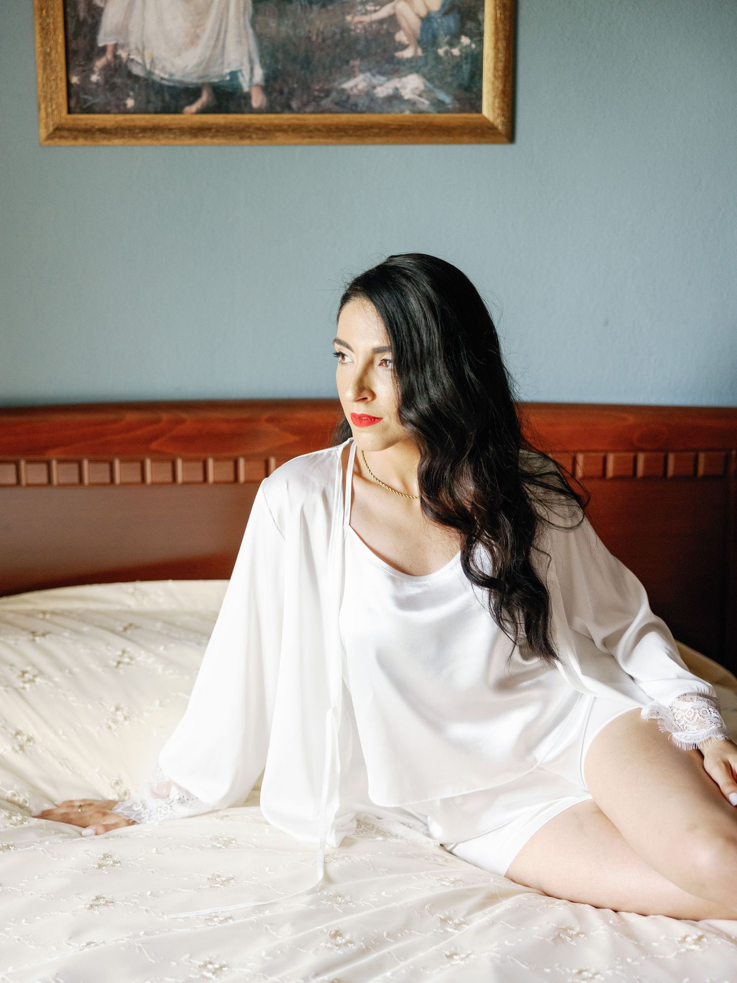 Artistic boudoir photography with white clothing against blue walls and vintage frames.