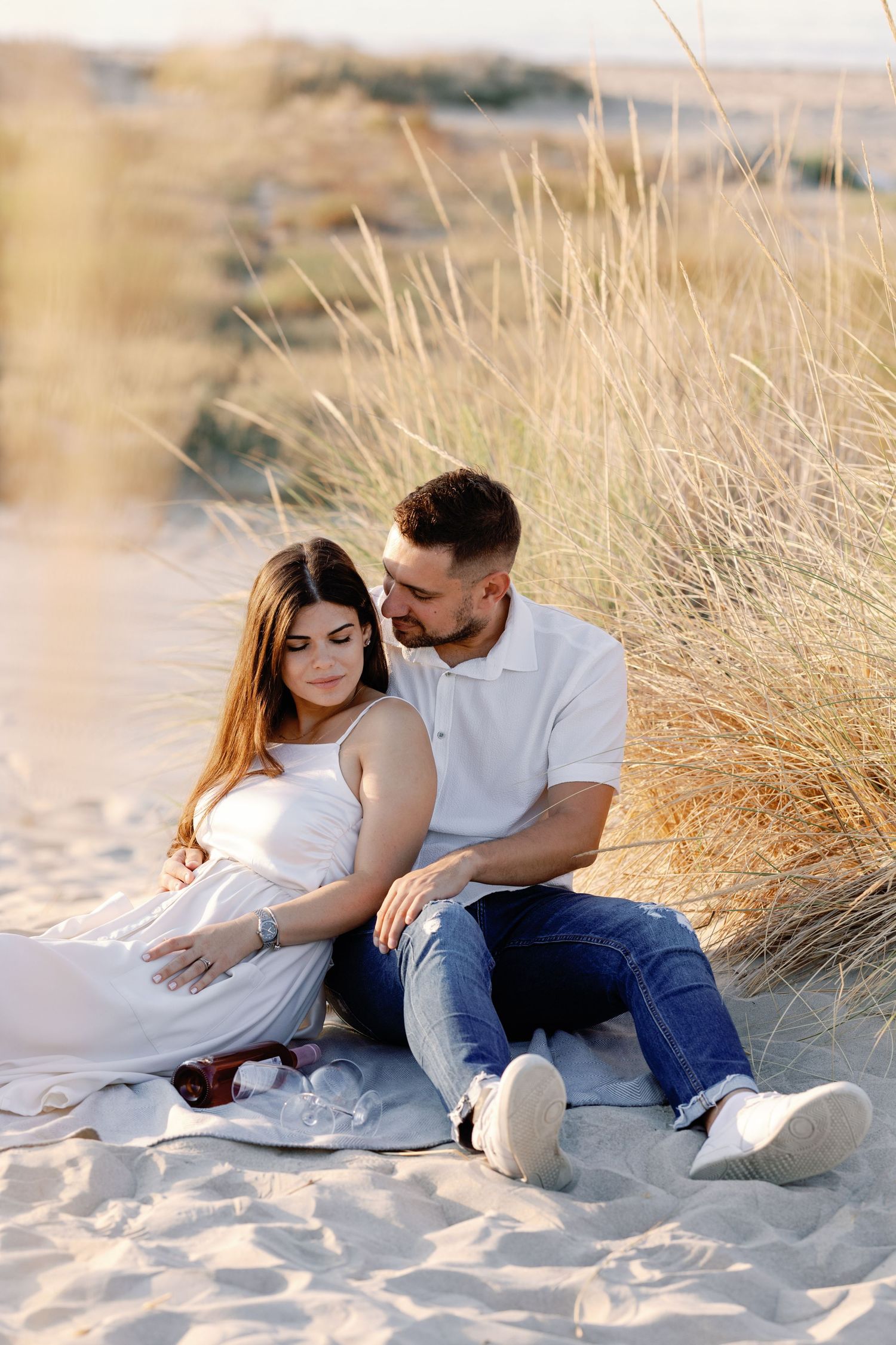 Couple sitting together on sandy beach surrounded by tall grass.