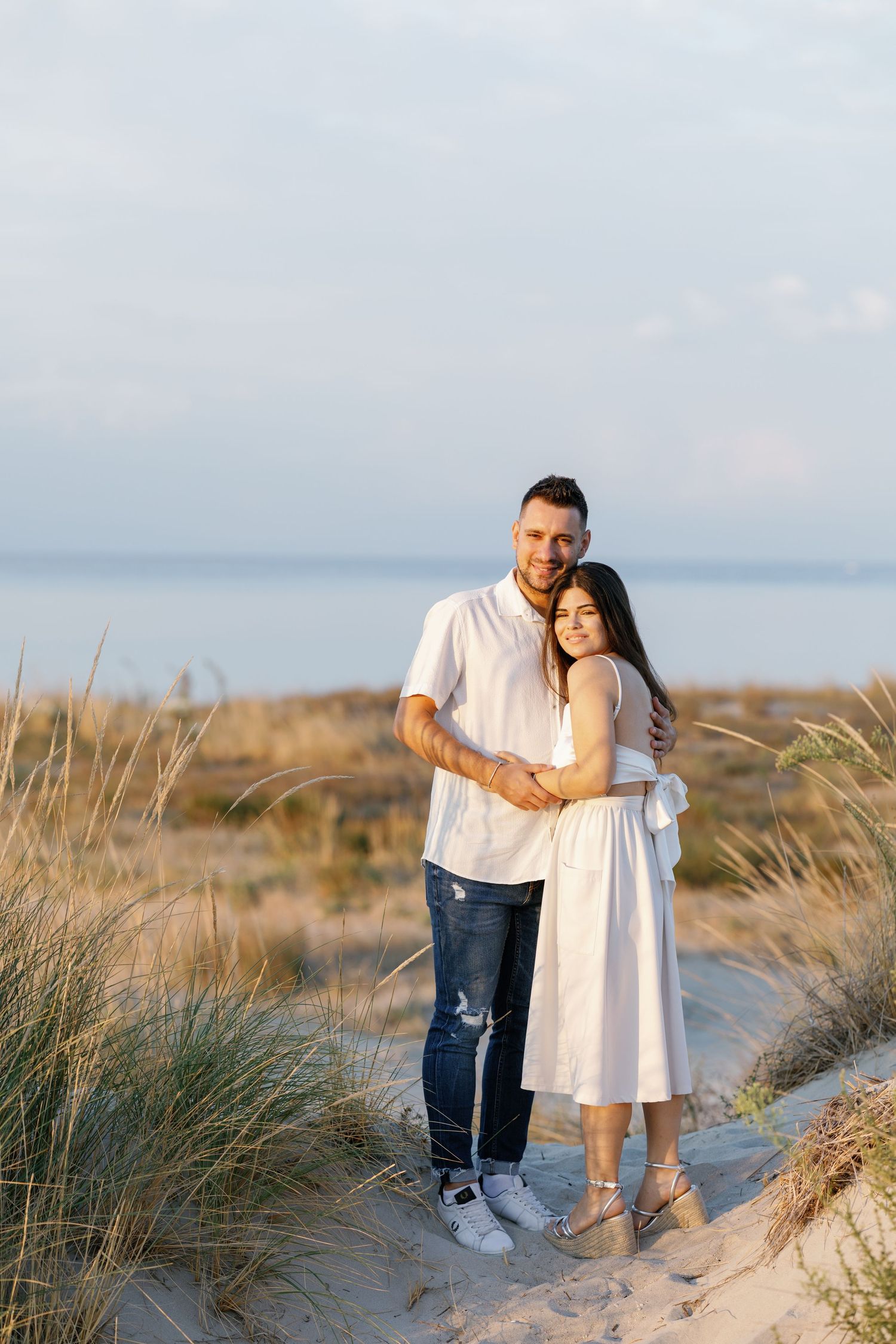 Couple walking together on sandy beach path with coastal grasses.