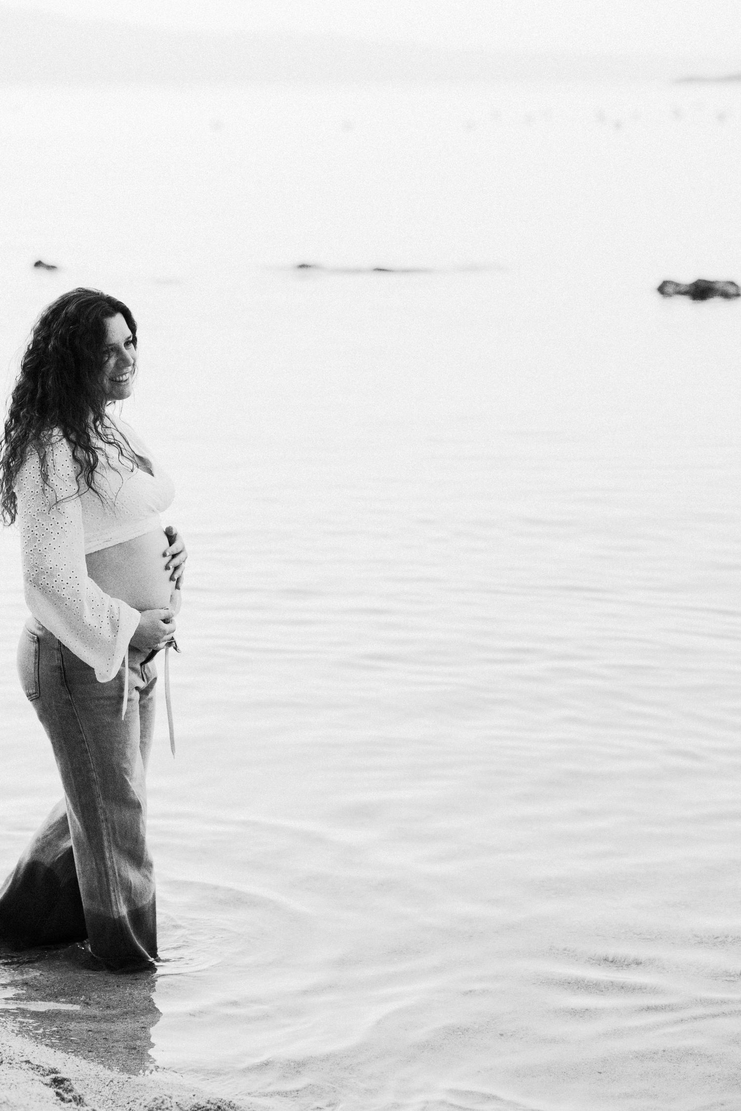 Black and white photos of expectant mother standing in calm waters during maternity shoot.