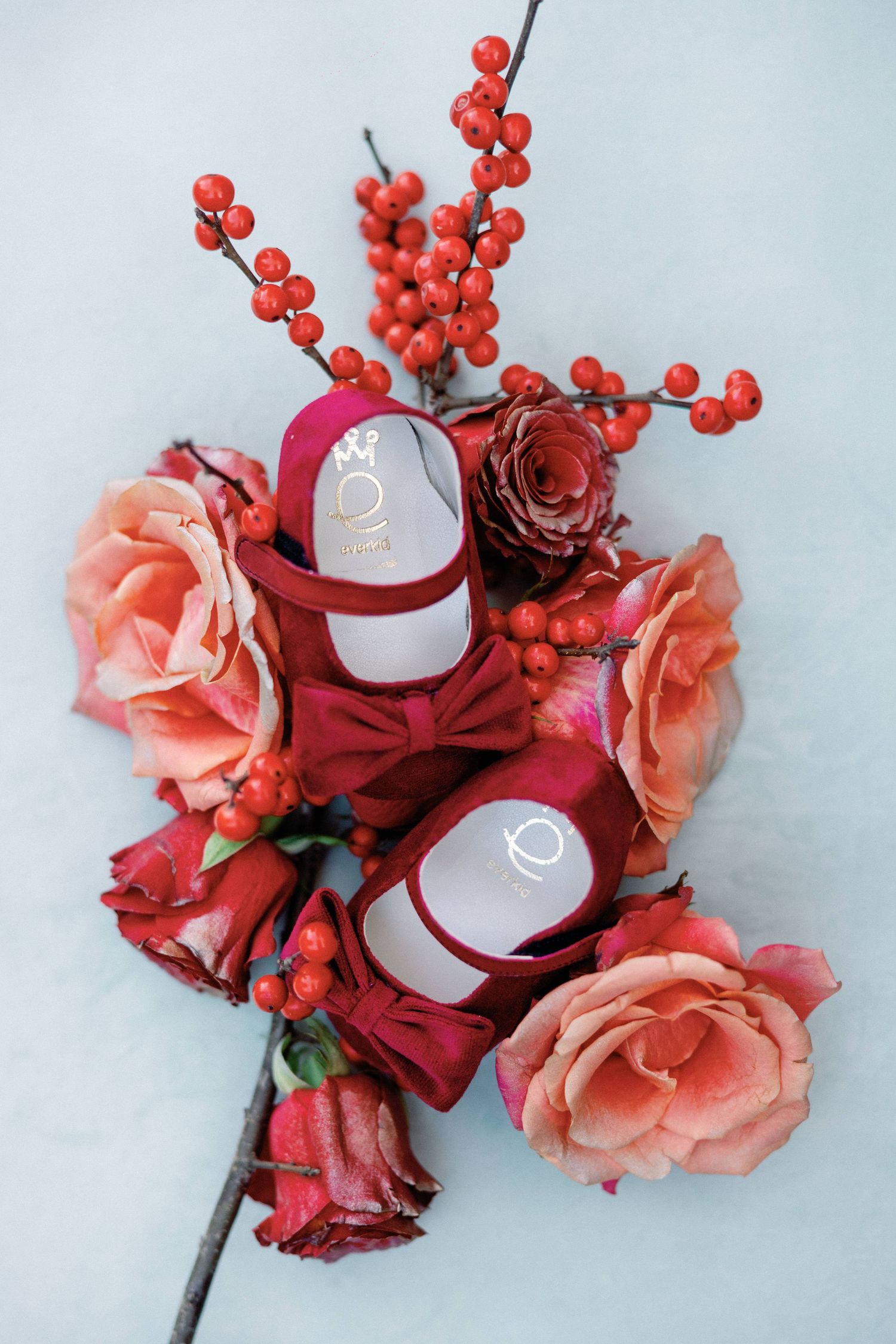 Elegant floral arrangement featuring deep red roses, peach-colored flowers, and bright red berries against a light background.