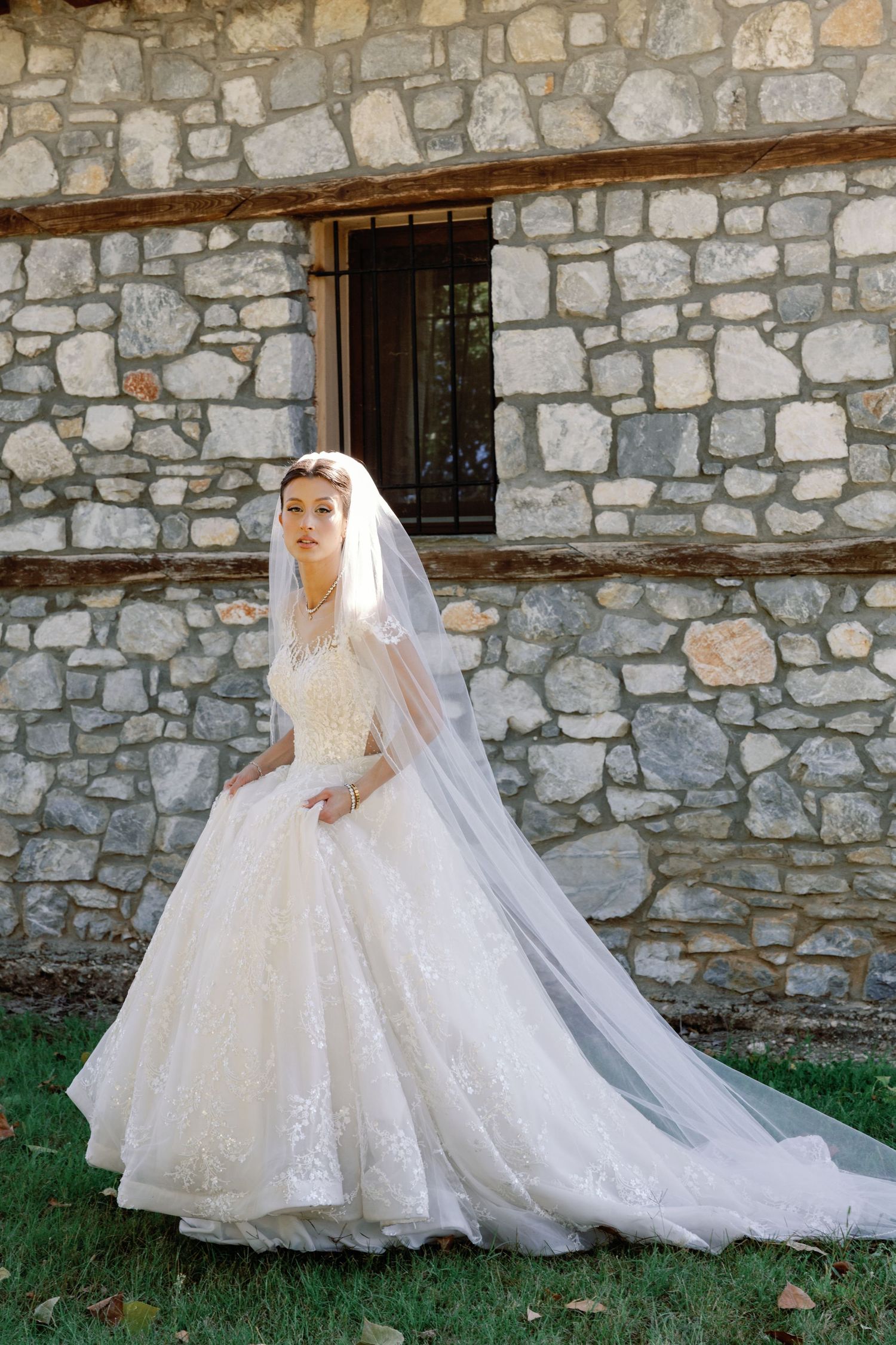 Stunning princess ball gown wedding dress photographed against a rustic stone wall backdrop.
