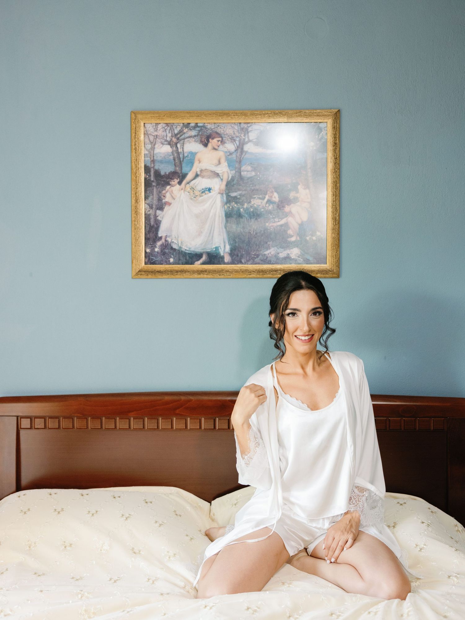 Boudoir photography session on white bedding with soft blue wall background.