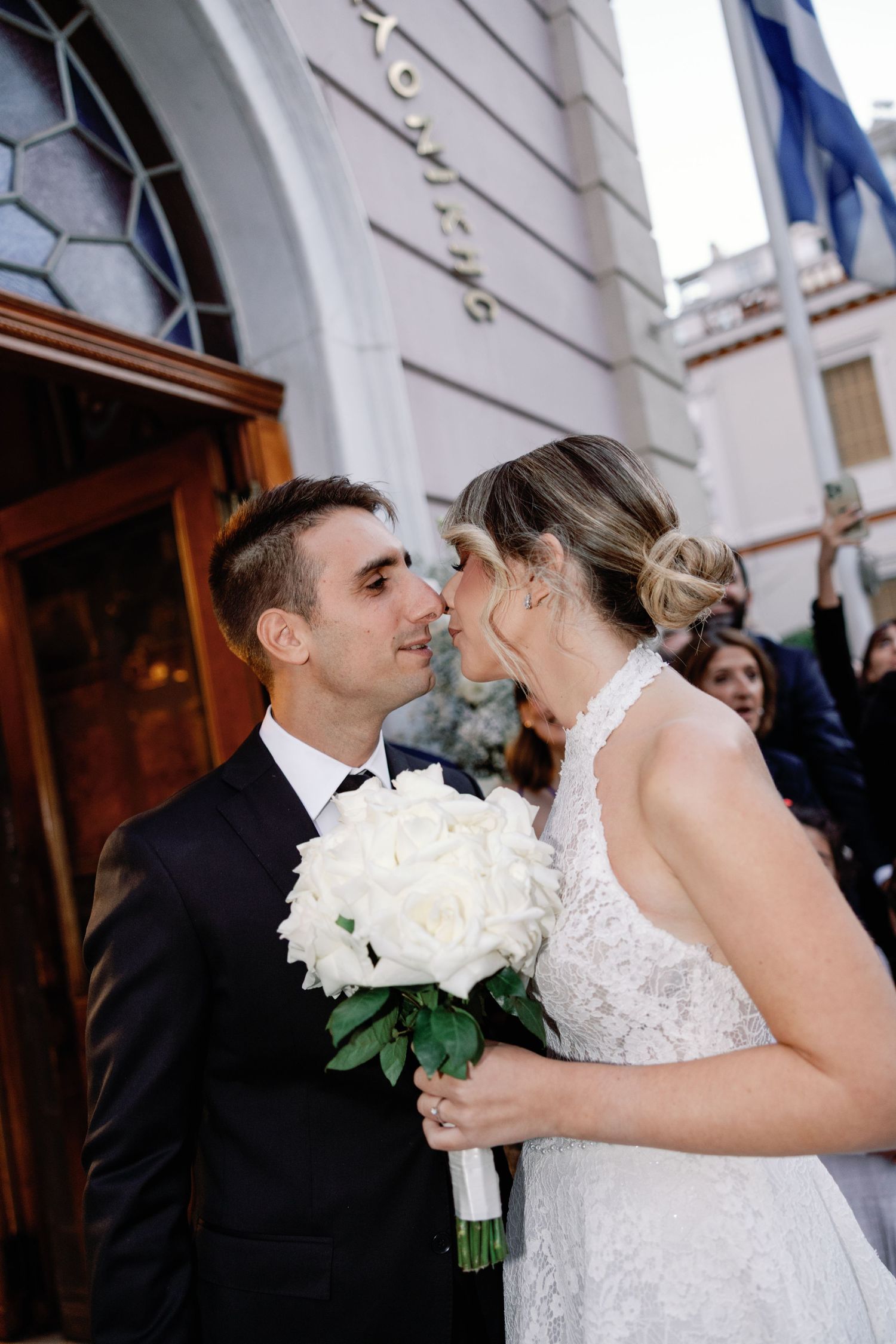 Bride holding white rose bouquet shares tender moment outside church.