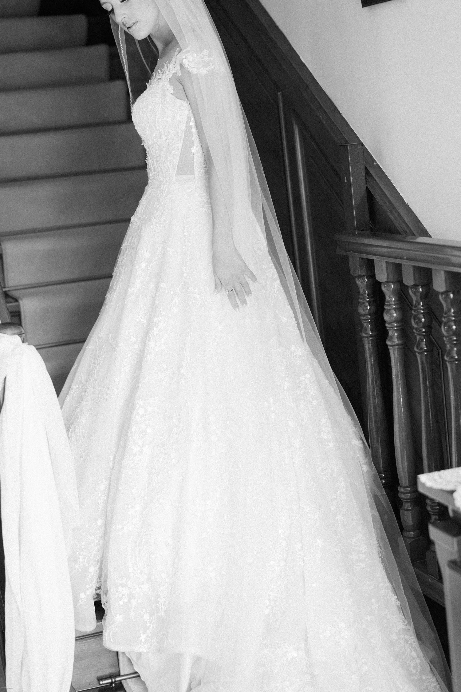 Wedding dress with lace details and flowing veil displayed on wooden staircase.