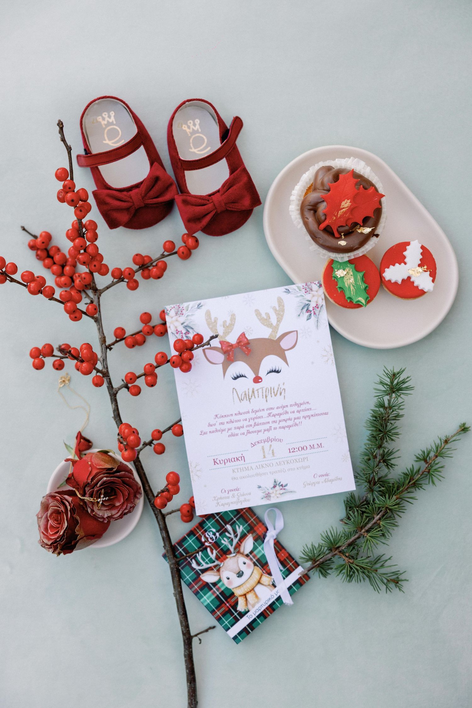 Festive Christmas flat lay with red berries, pine sprigs, candy canes and greeting cards on a light blue background.